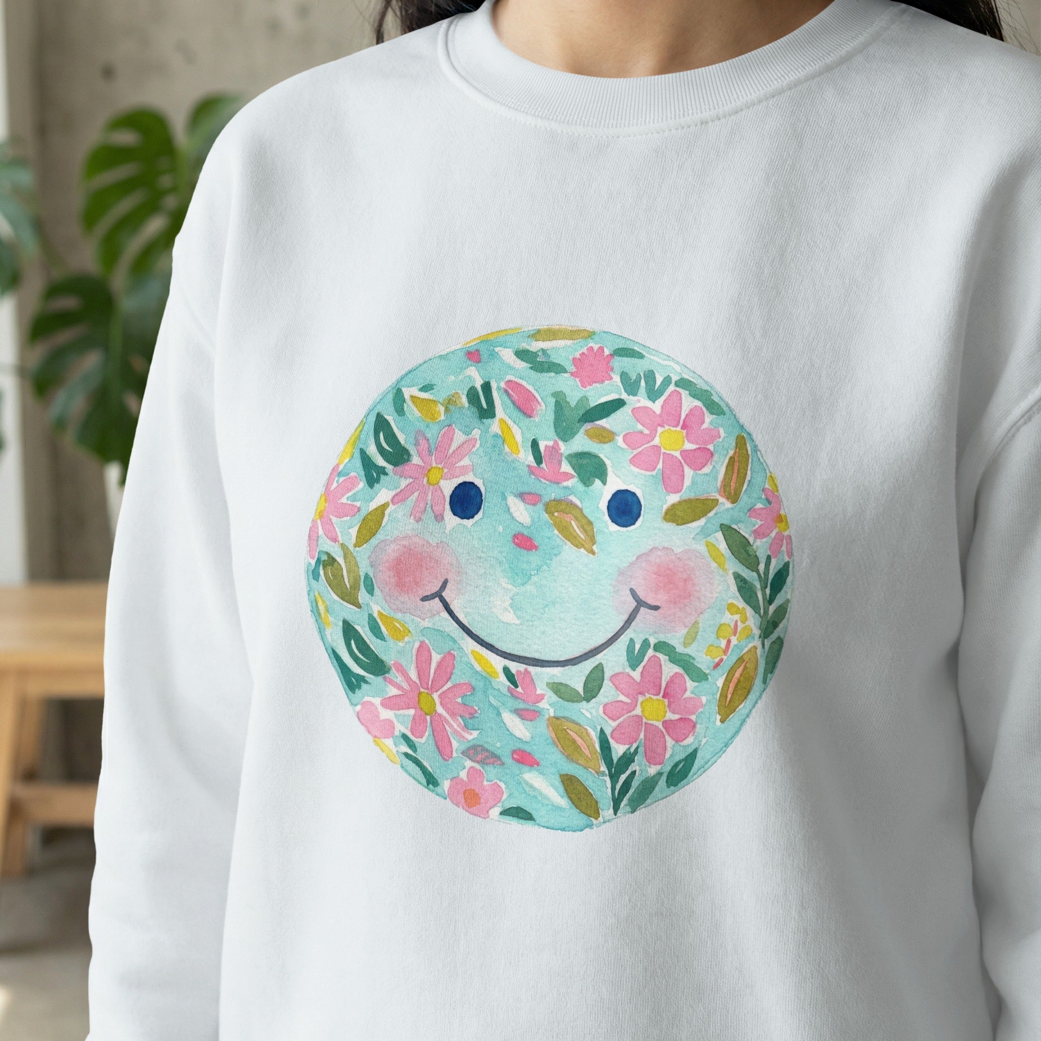 White sweatshirt with a watercolor smiley face composed of flowers and leaves.