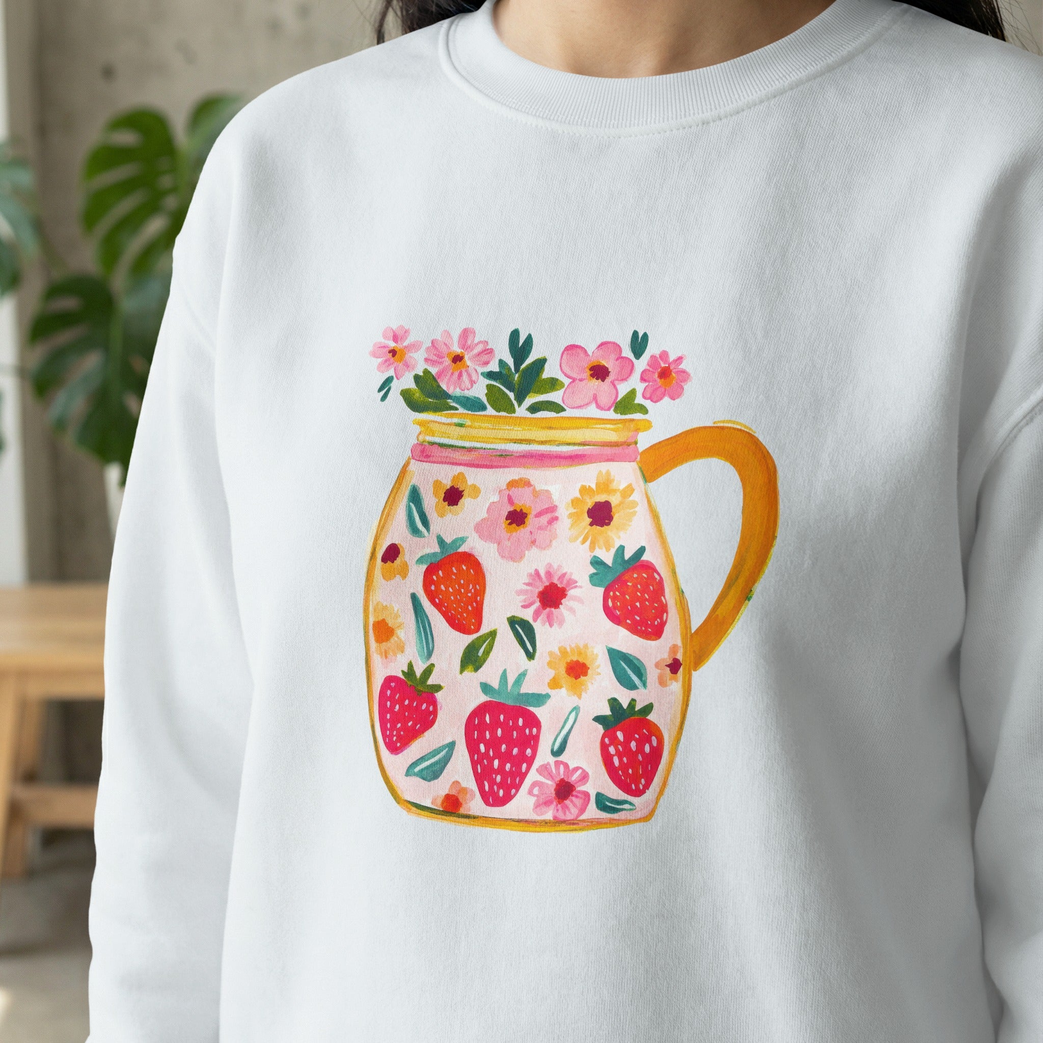 White sweatshirt with a colorful strawberry and floral jar design.