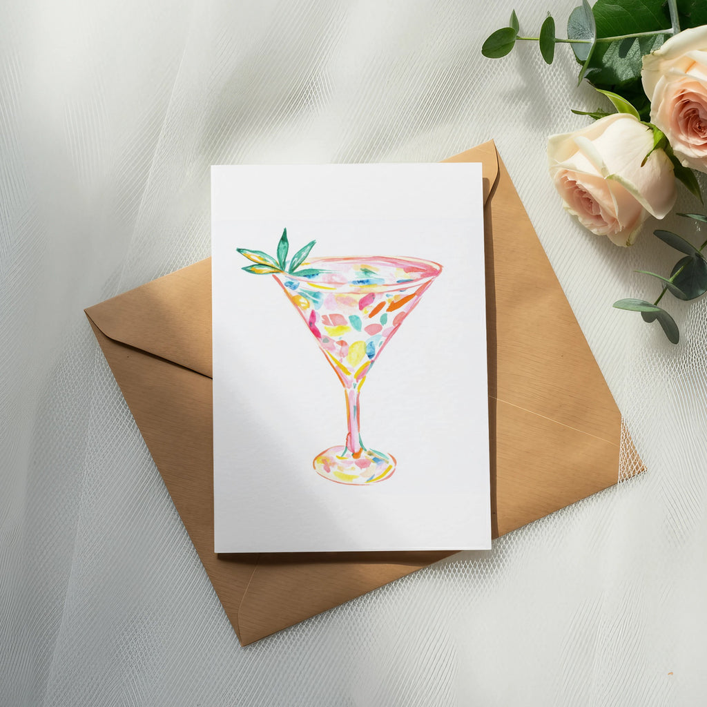 Watercolor cocktail glass with colorful splashes on white cardstock atop a brown envelope.