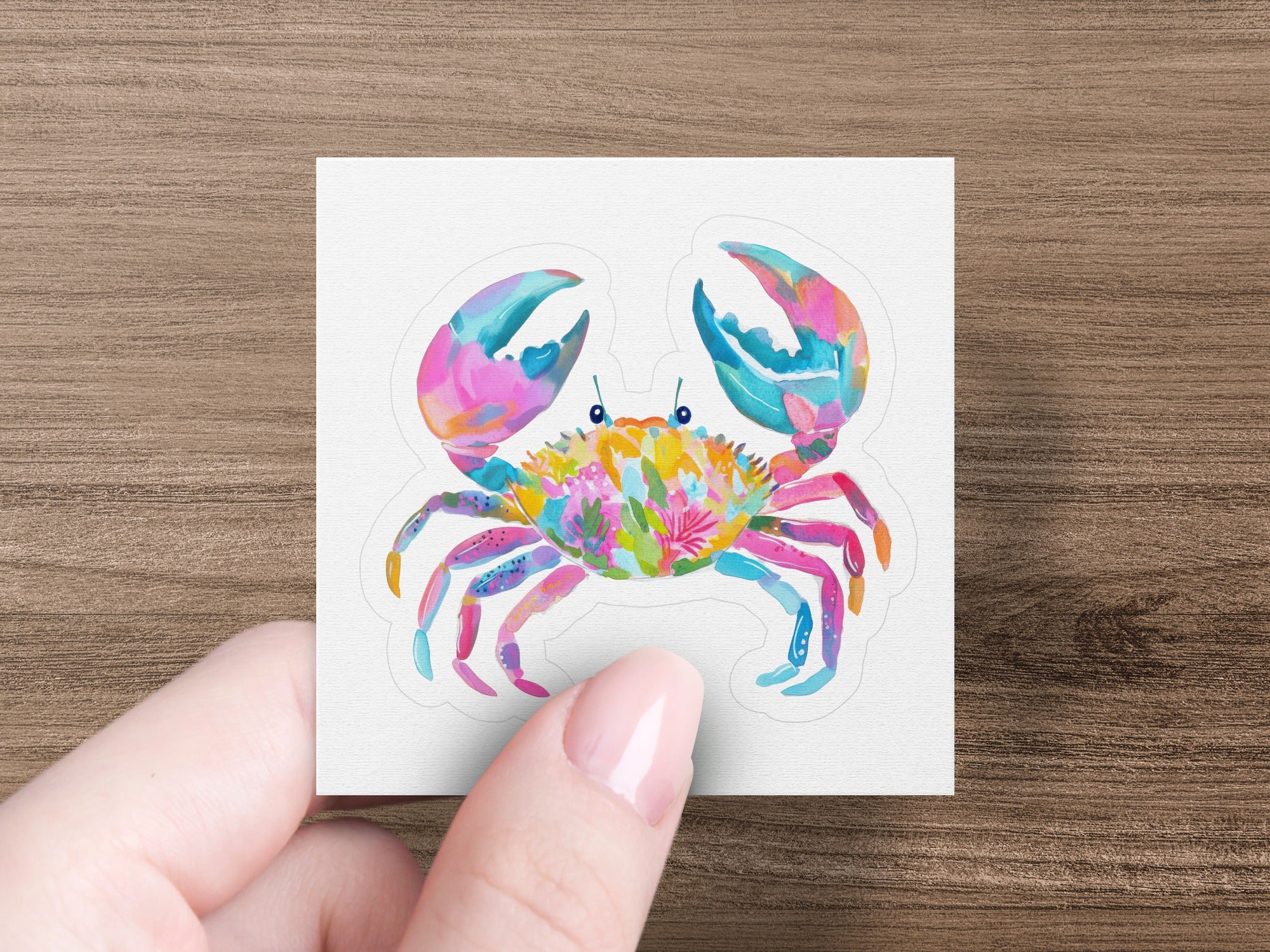 Colorful crab illustration with floral accents held by a hand.