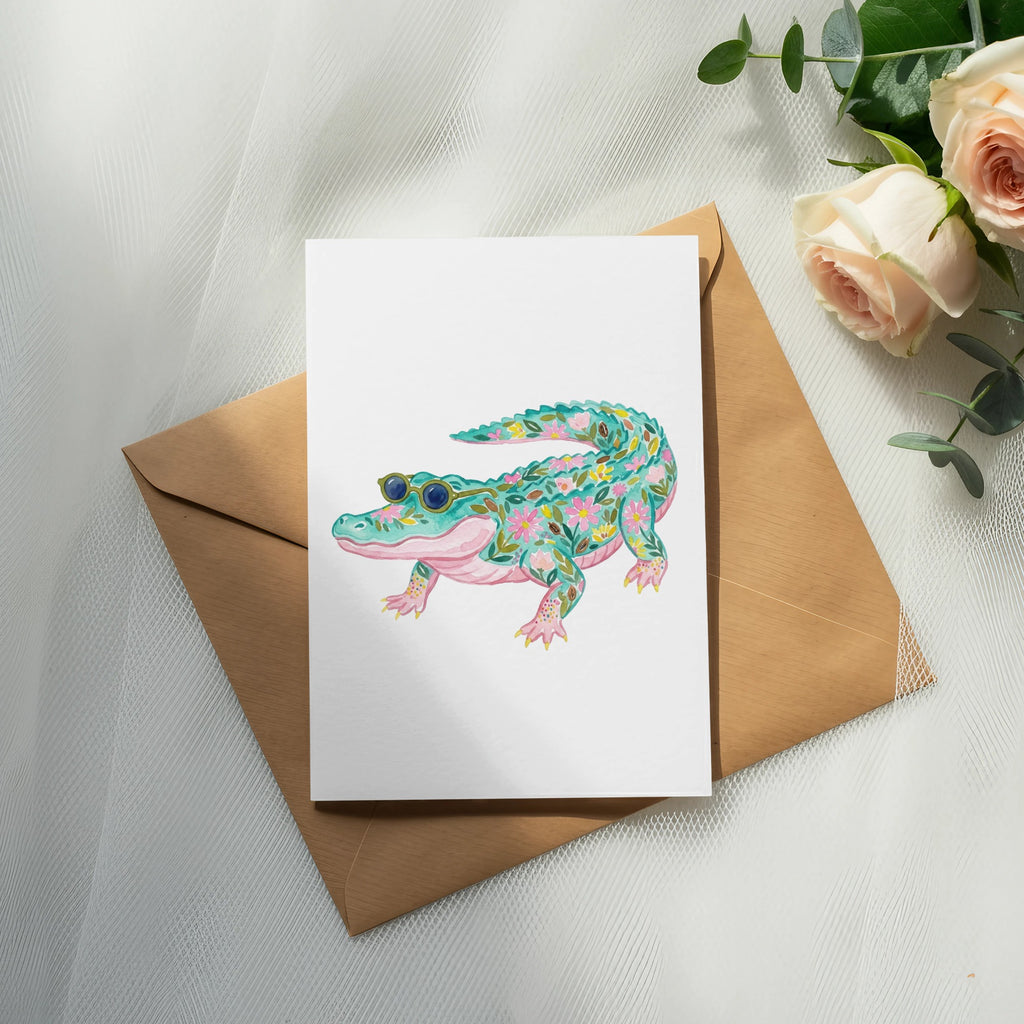 Watercolor alligator with floral pattern wearing sunglasses on a card.