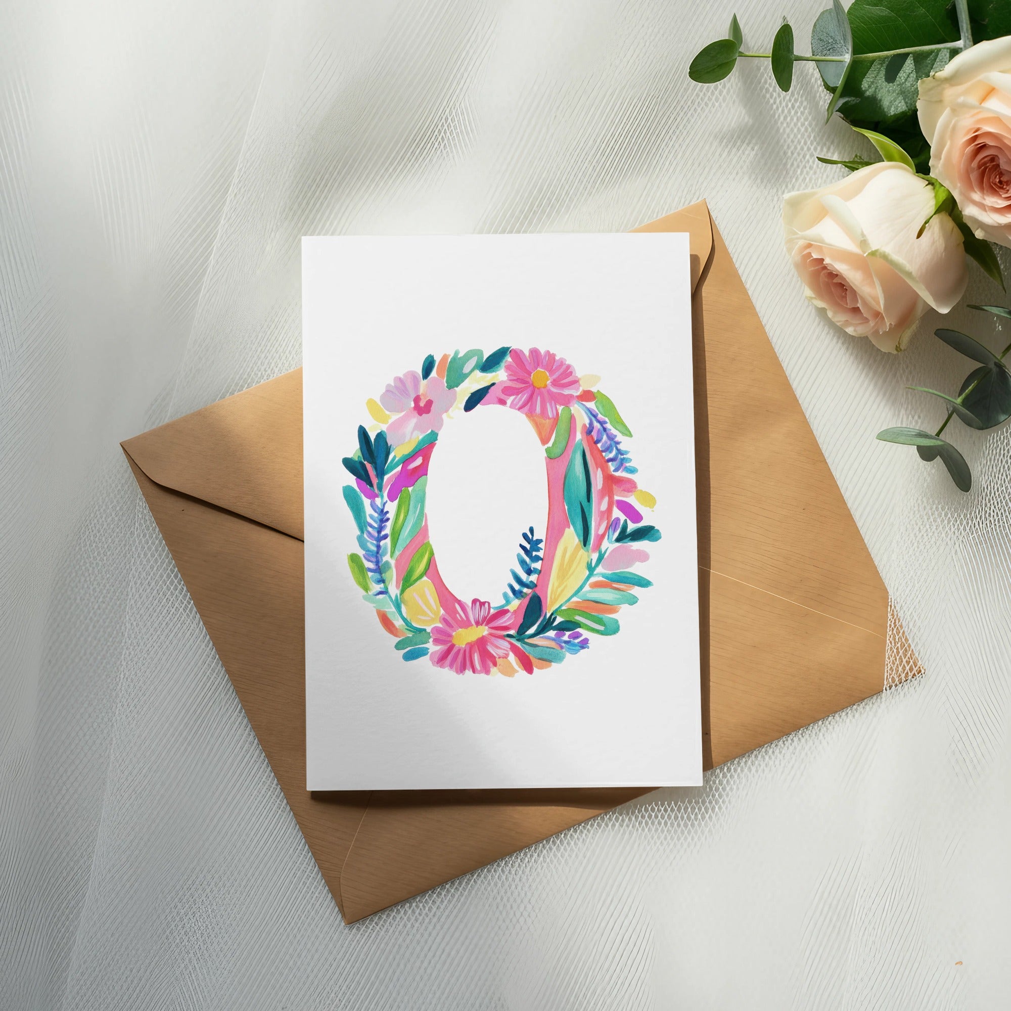 Watercolor letter O surrounded by flowers on a card, with an envelope and roses.