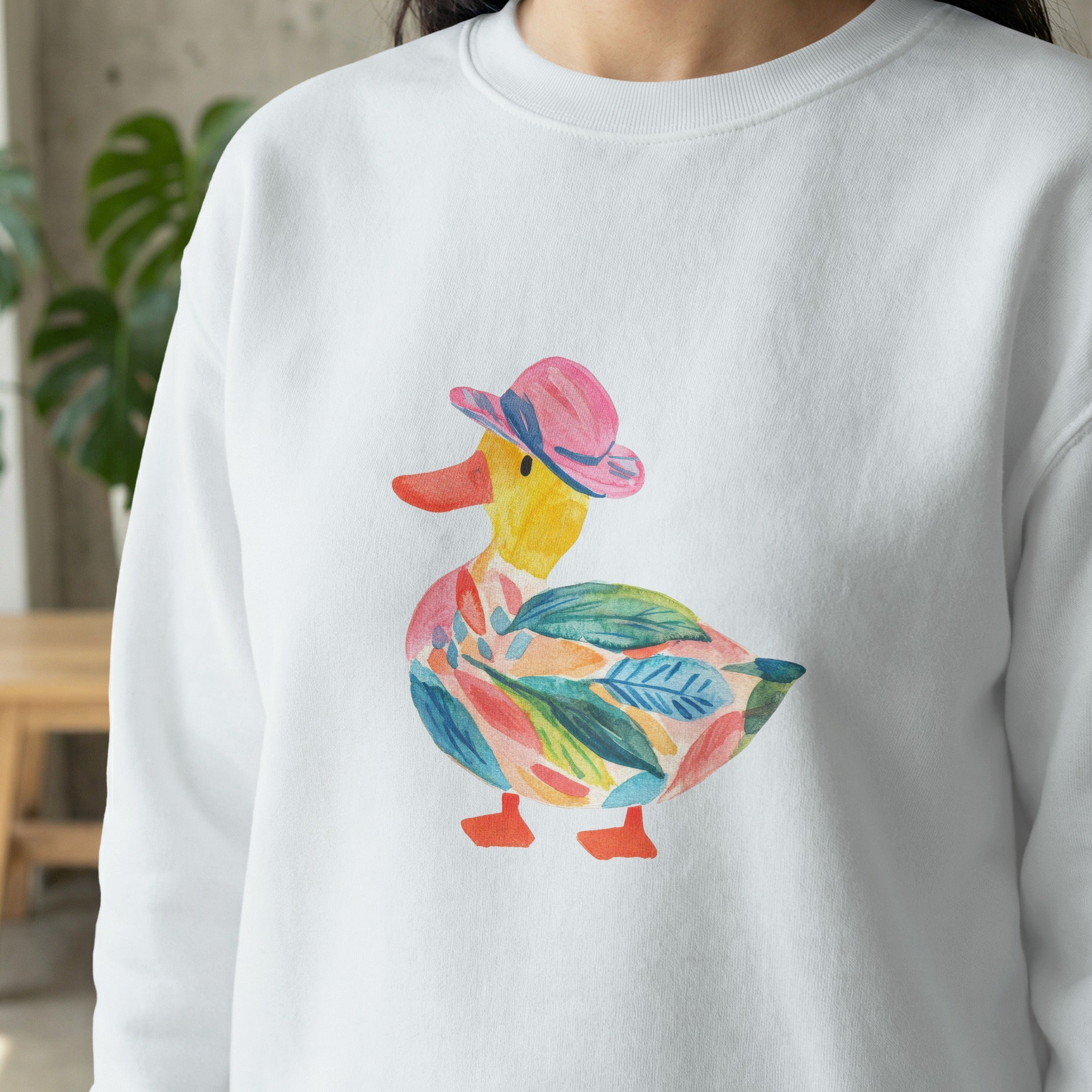 White sweatshirt with colorful watercolor duck wearing a pink hat.