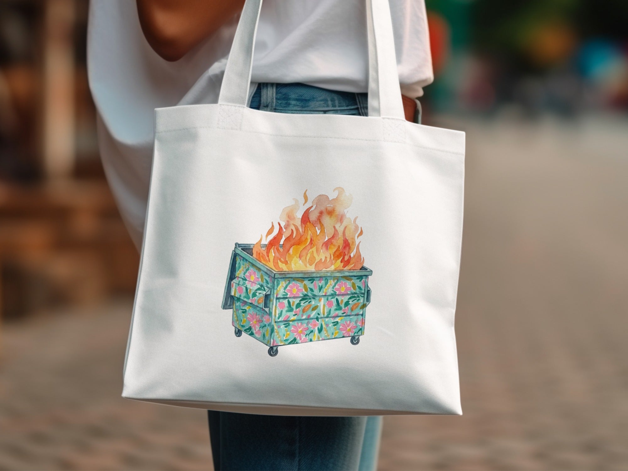 White canvas tote bag with a dumpster fire illustration and floral accents.
