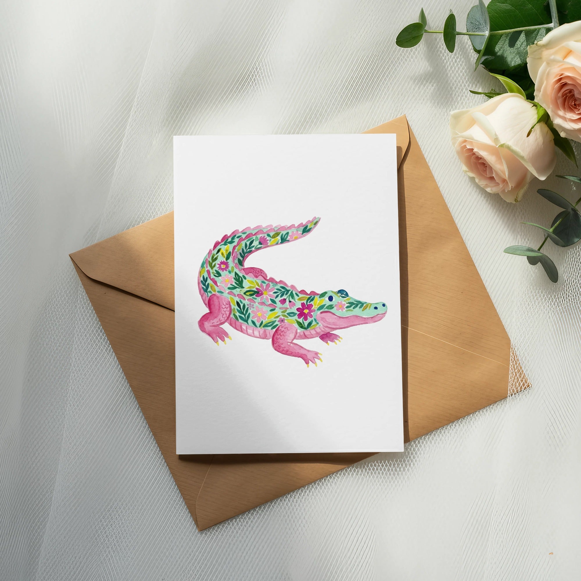 Watercolor alligator illustration with floral patterns on a card, atop an envelope.