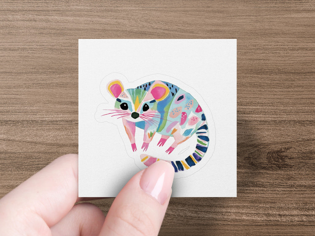 Stylized possum sticker with colorful abstract patterns on a wood background.