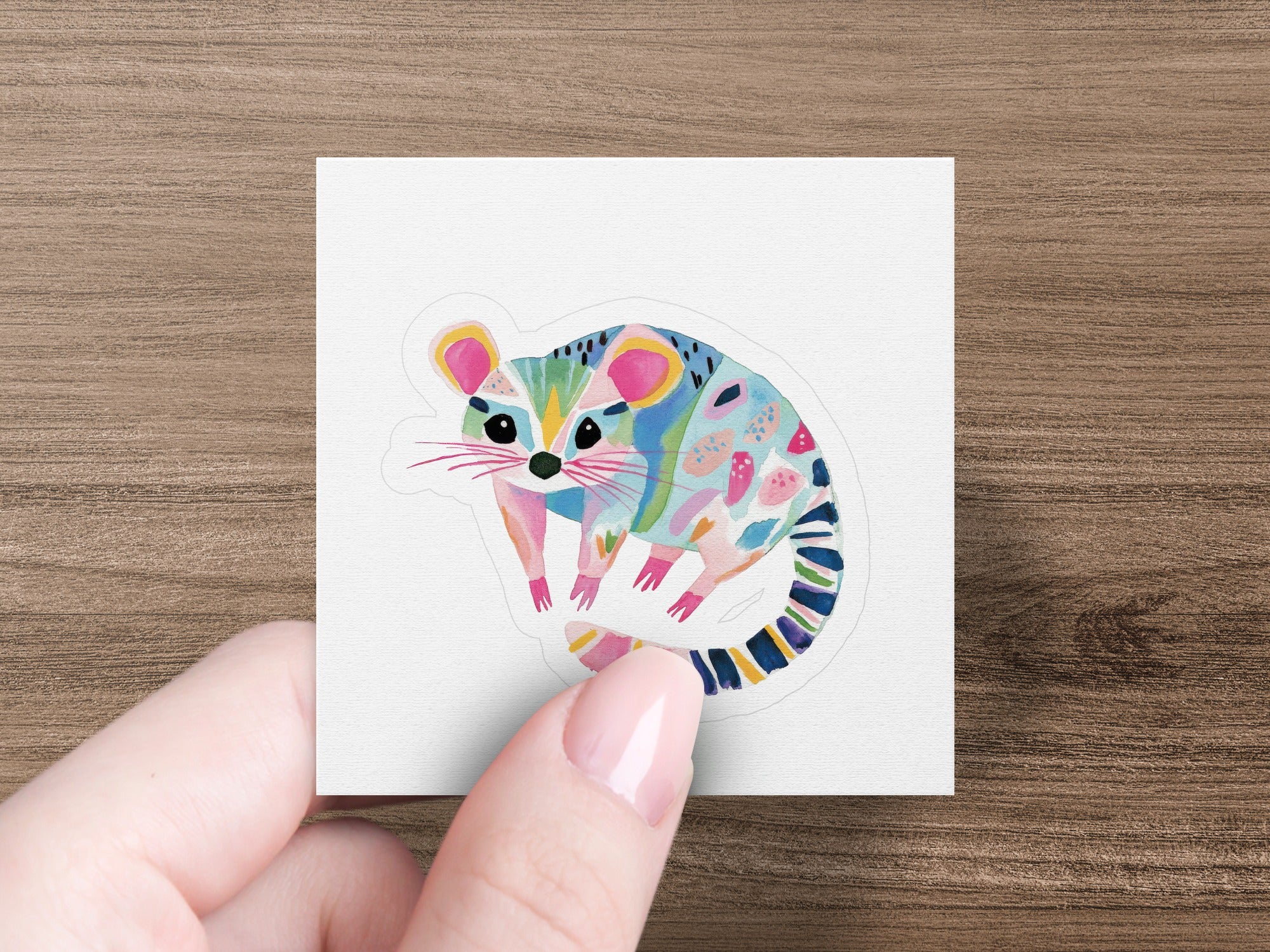 Stylized possum sticker with colorful abstract patterns on a wood background.