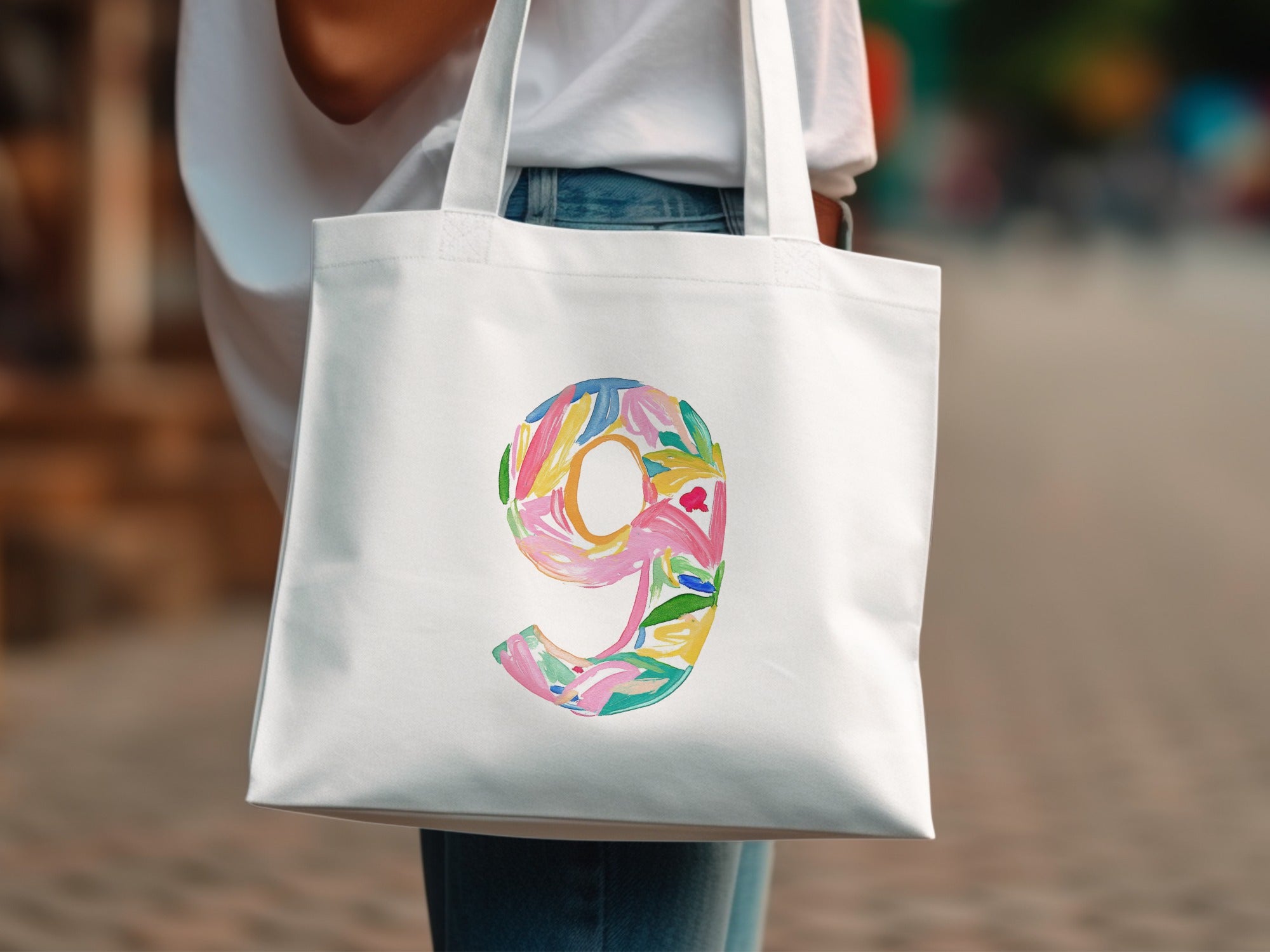 White tote bag with a colorful watercolor number 9 design.