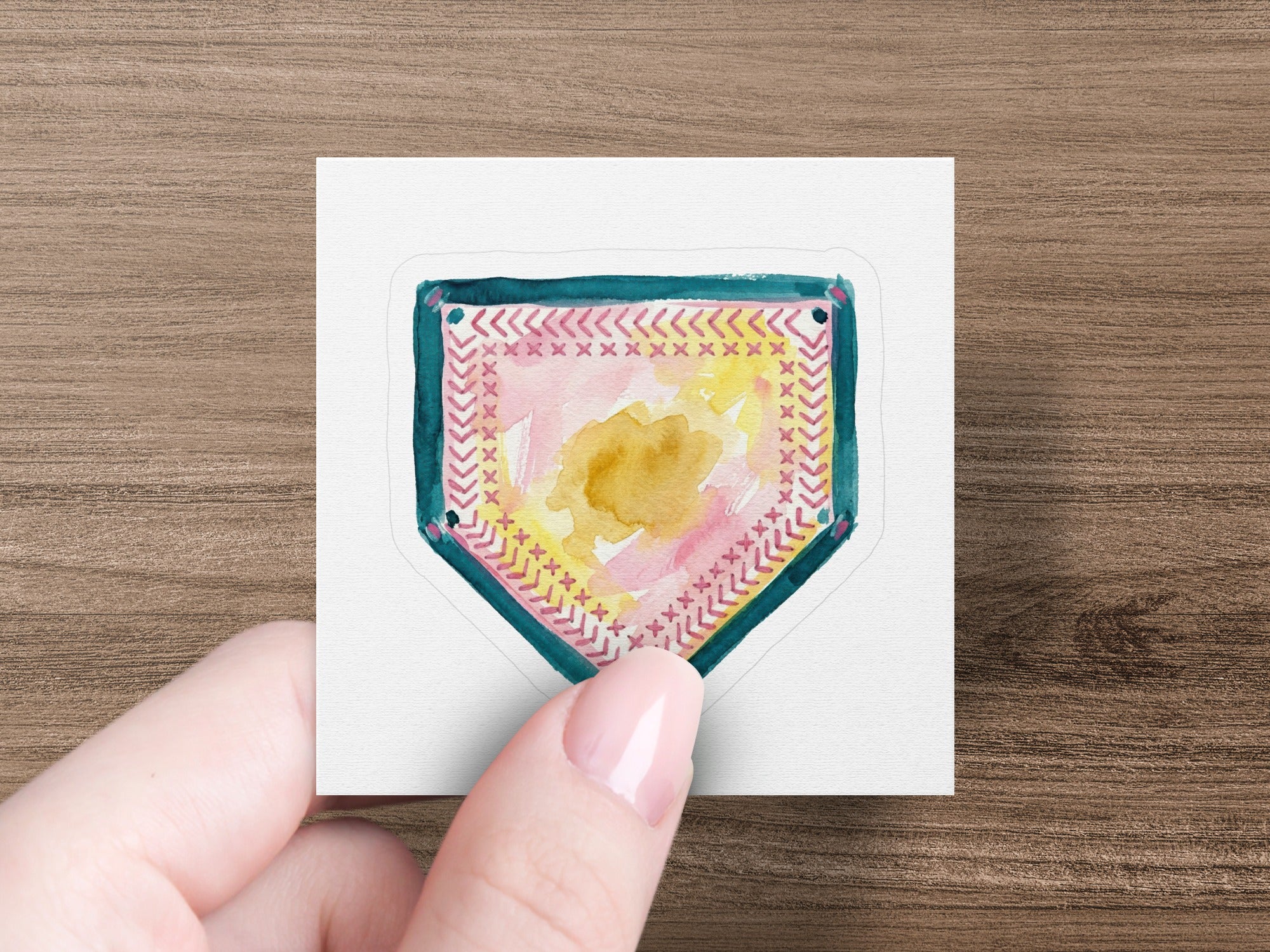 Shield-shaped sticker with pink and yellow abstract watercolor design, bordered by teal stitching.