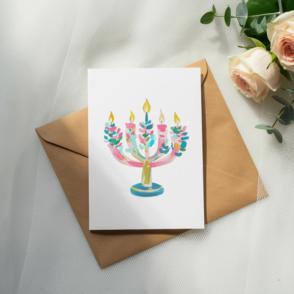 Watercolor illustration of a pink and blue menorah on a white card.