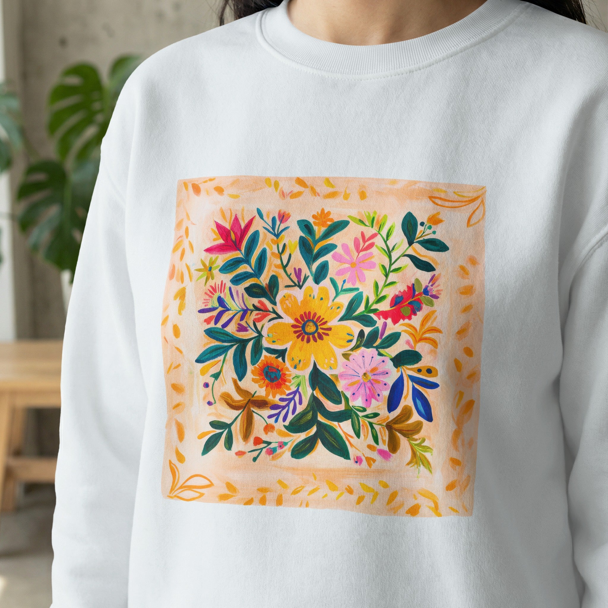 White sweatshirt with a square floral illustration featuring a colorful arrangement of flowers and leaves.