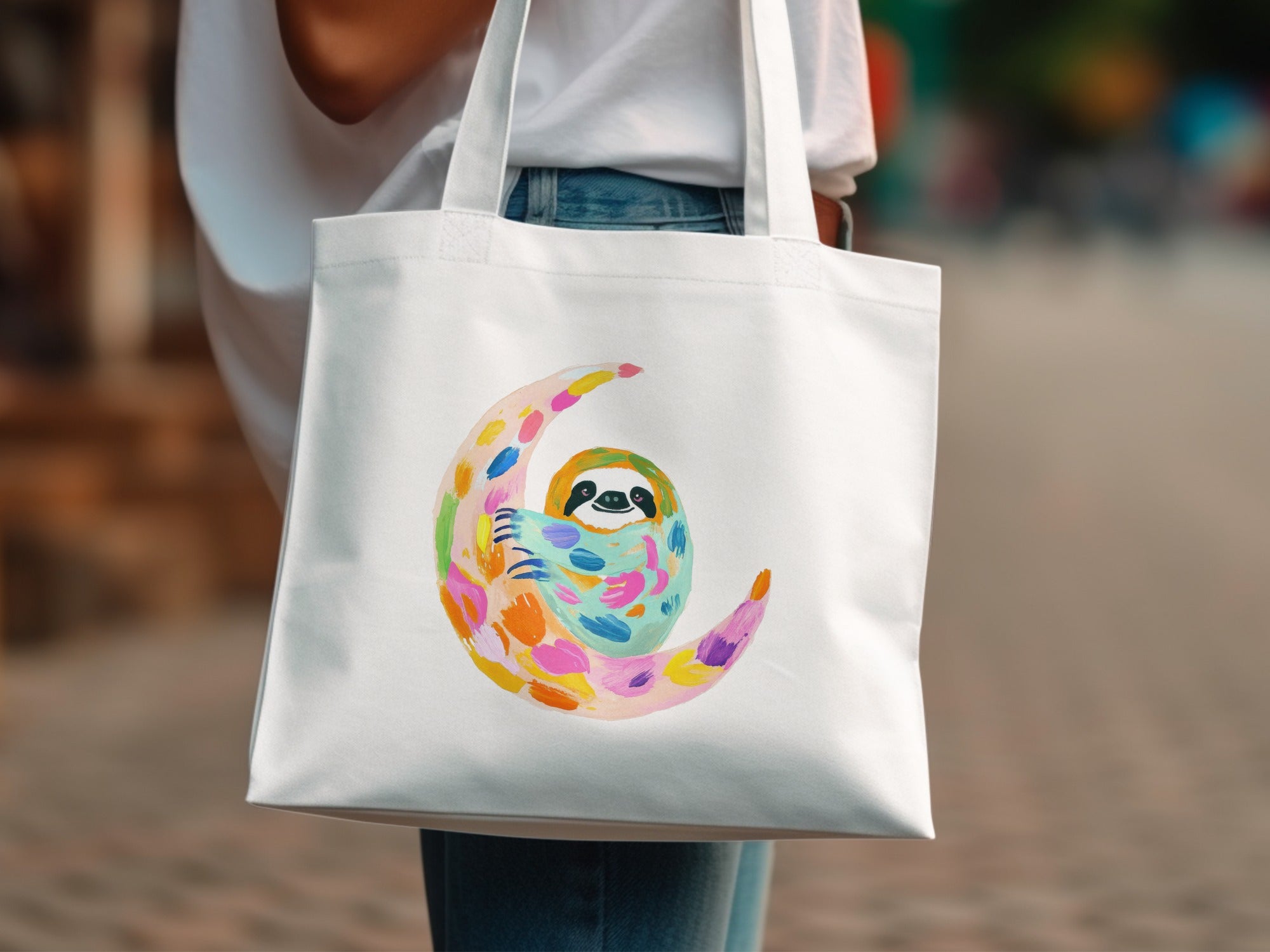 White tote bag with a colorful moon and sloth illustration.