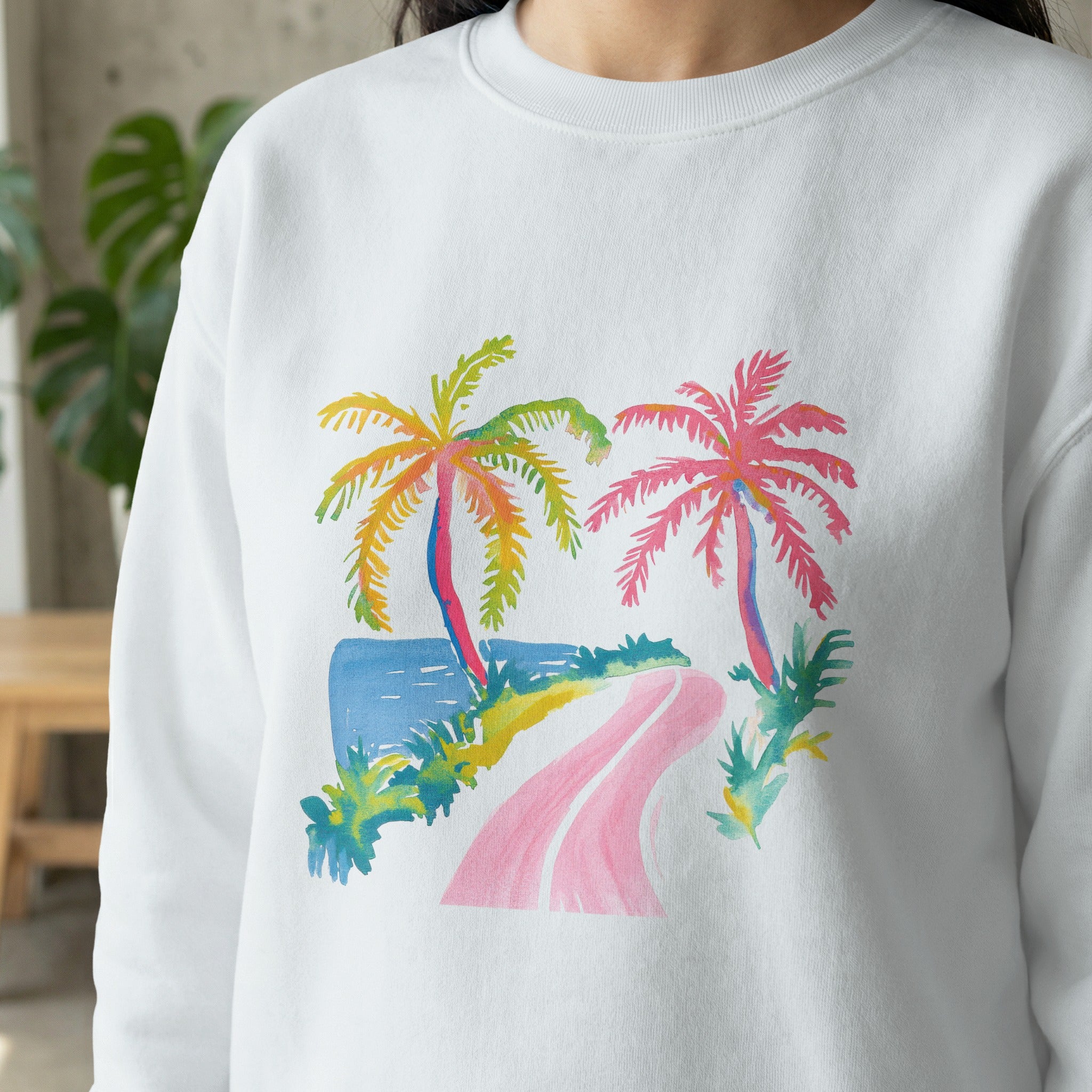 White sweatshirt with watercolor painting of two palm trees and a road.