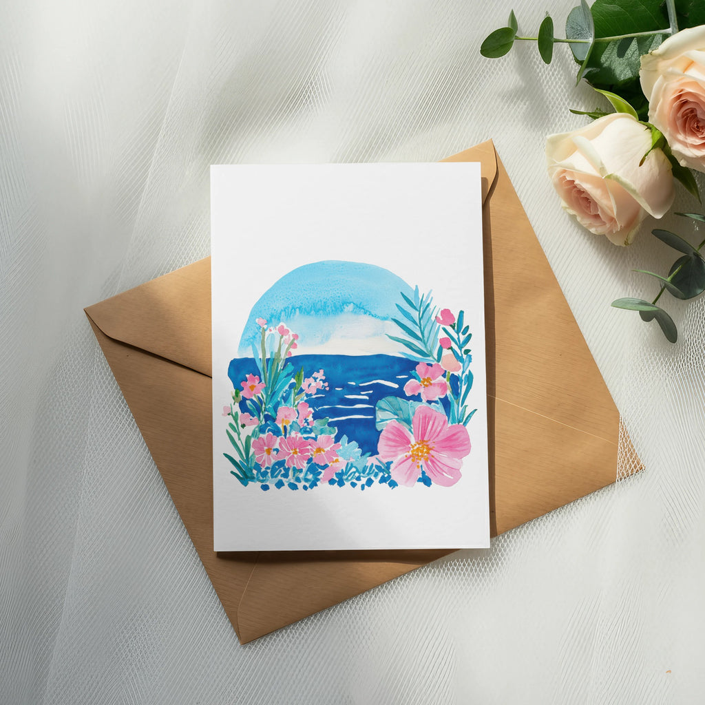 Watercolor floral and ocean scene on greeting card atop a brown envelope.