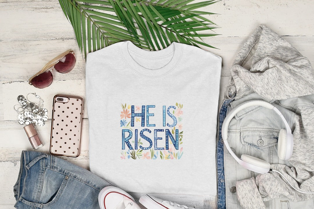White t-shirt with "He Is Risen" text and floral design.