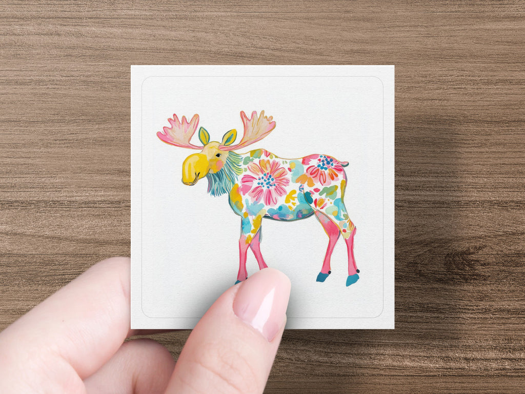 Moose illustration with floral pattern on white square held by hand.