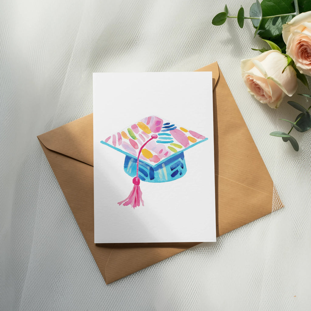 Watercolor graduation cap illustration on a card, next to a kraft envelope and roses.