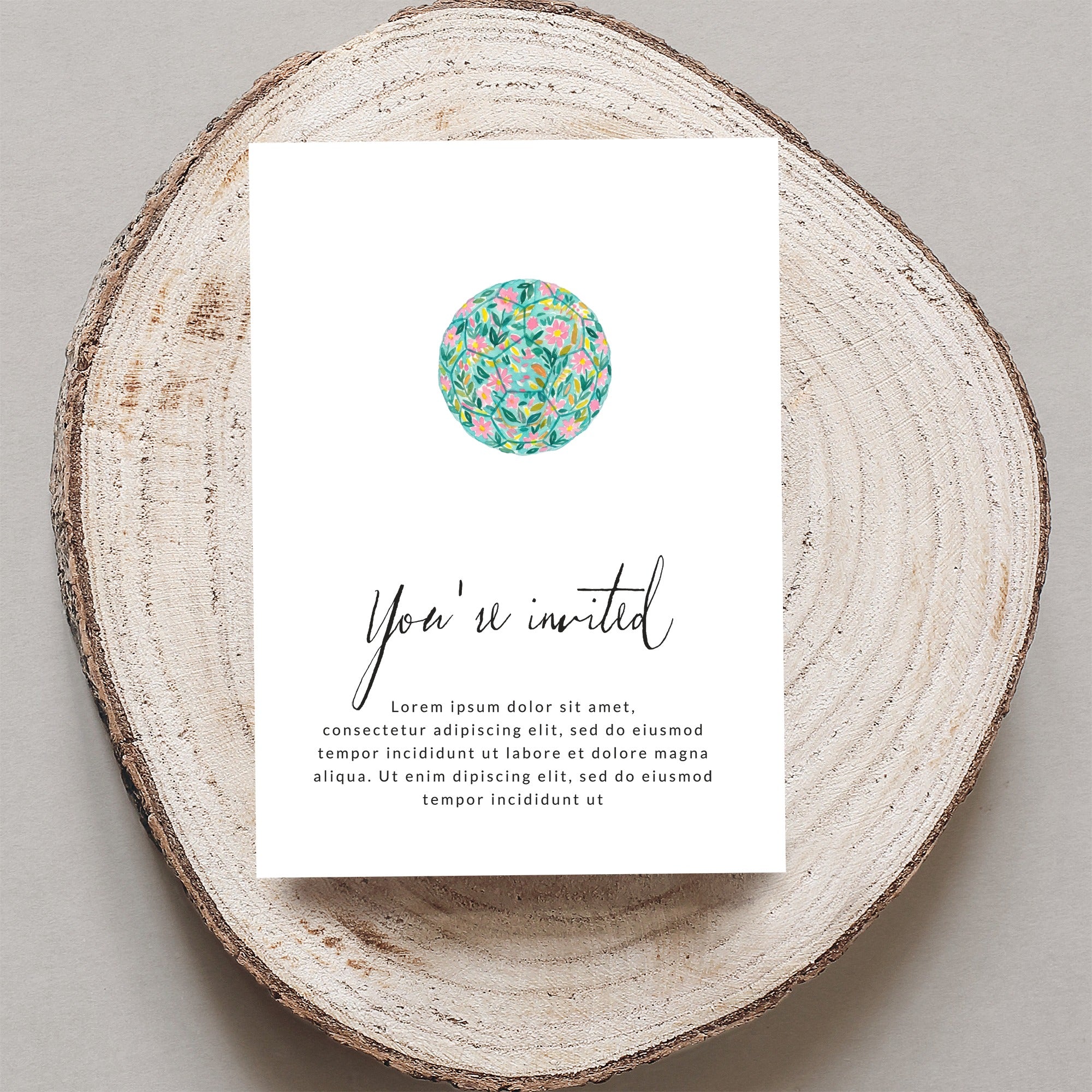 Invitation card with floral design and placeholder text, on a wood slice.