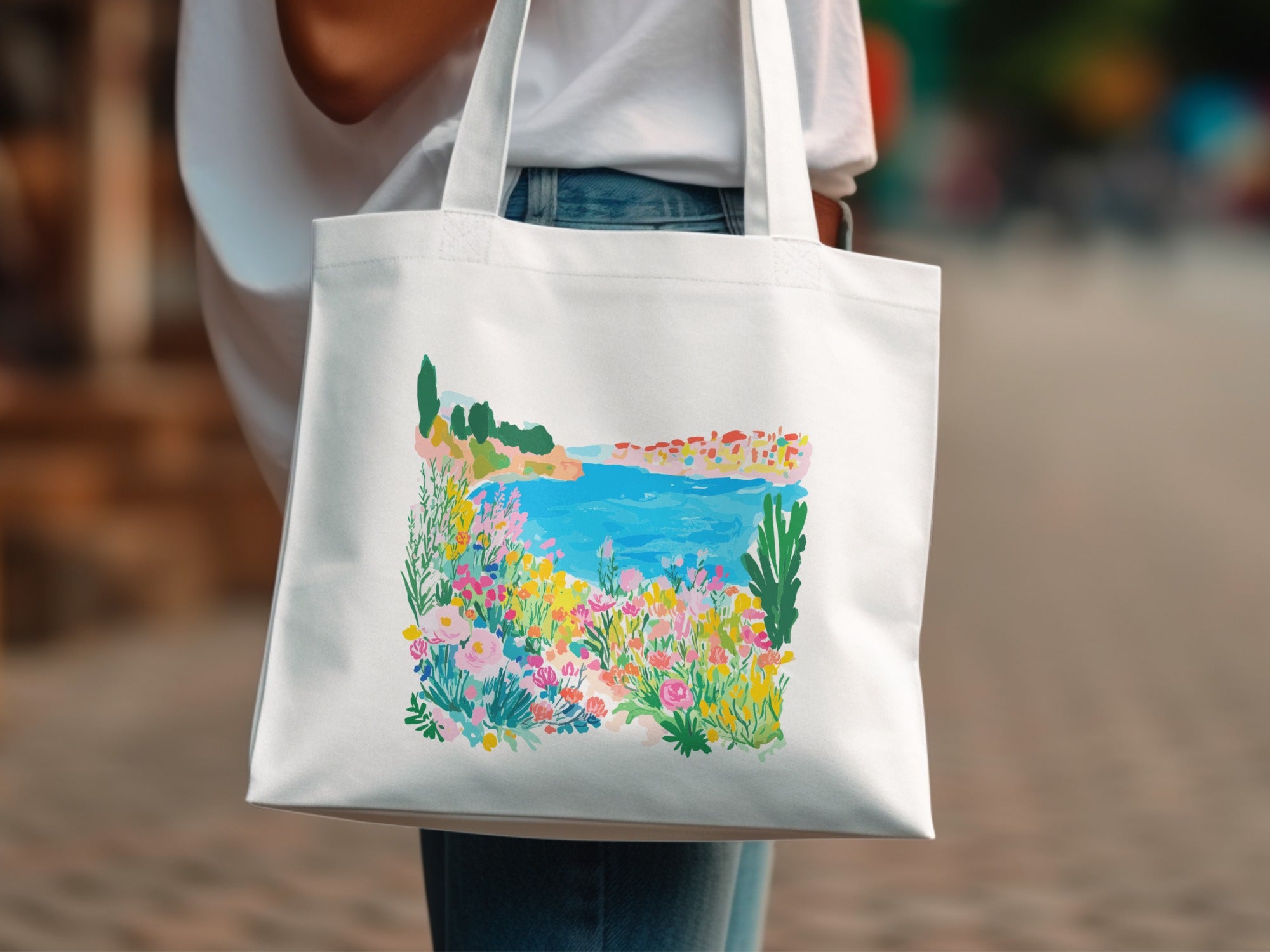 White tote bag with a colorful watercolor landscape of a coastal town.