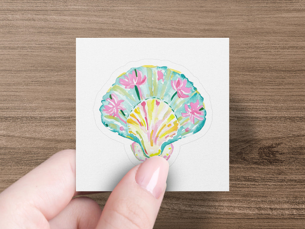 Colorful seashell sticker with pink flowers, held by a hand.