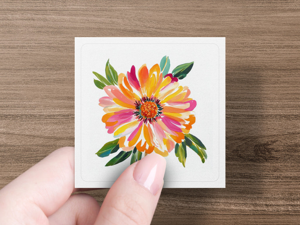 Hand holding square card with vibrant floral painting of a dahlia.