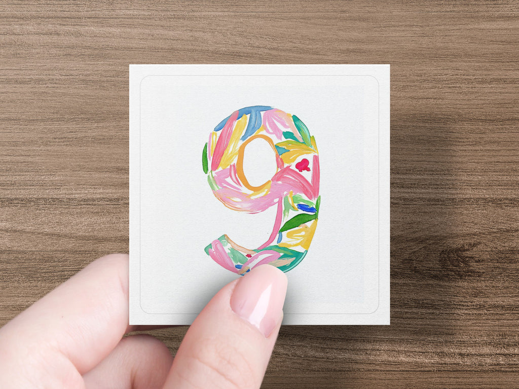Colorful floral number nine on white card held by hand.