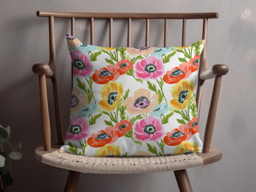 Floral pillow with pink, orange, and yellow poppies on a wooden chair.