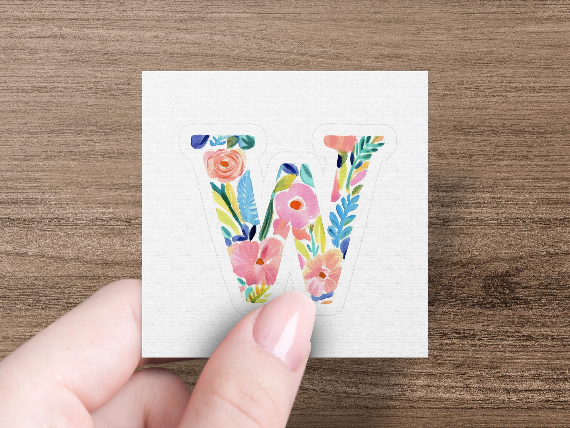 Watercolor letter W with colorful floral accents held by a hand.