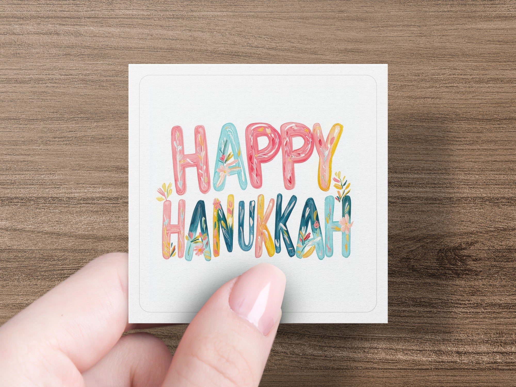 Hand holding card with "Happy Hanukkah" in colorful, stylized lettering.