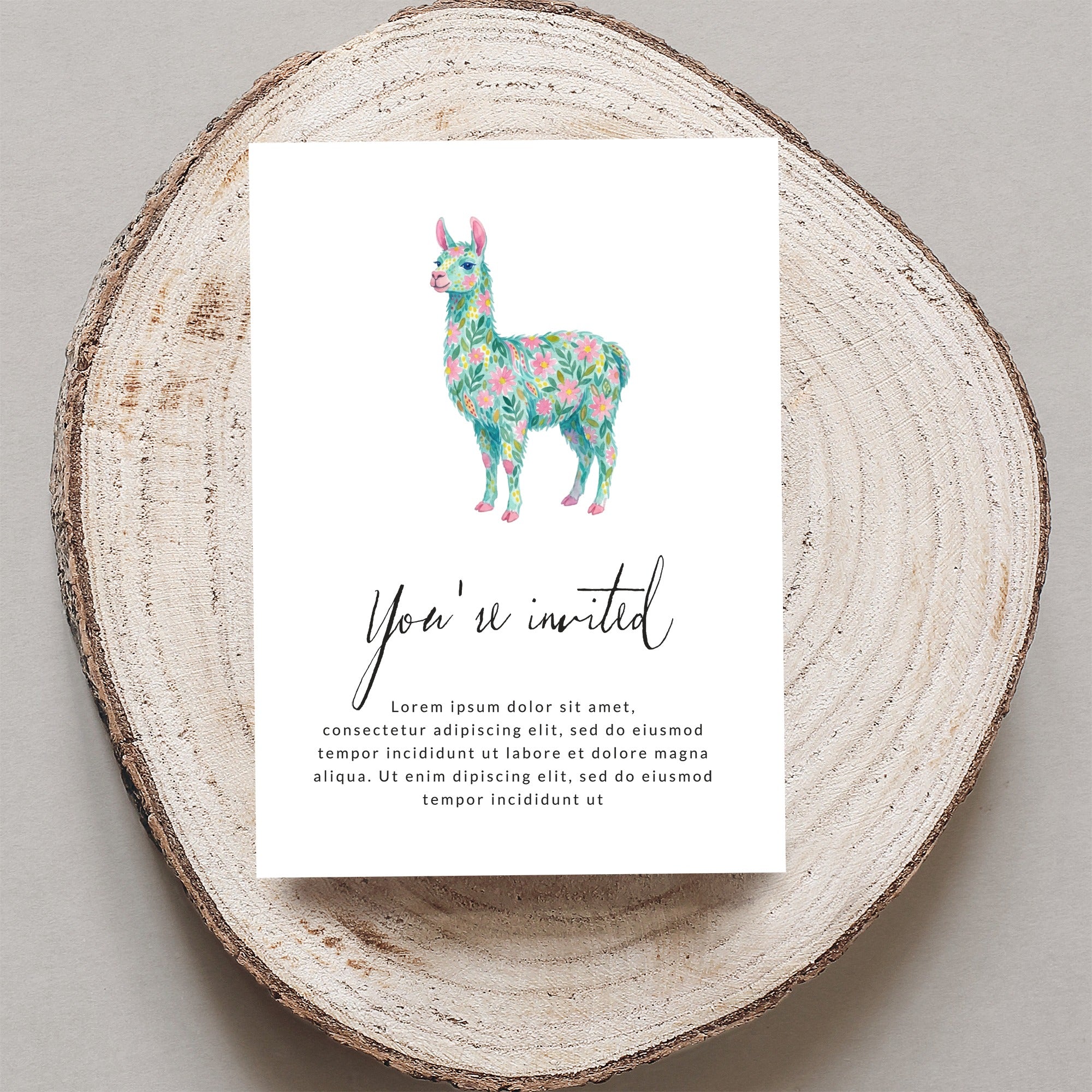 Card with floral llama and "You're invited" text on wood slice.