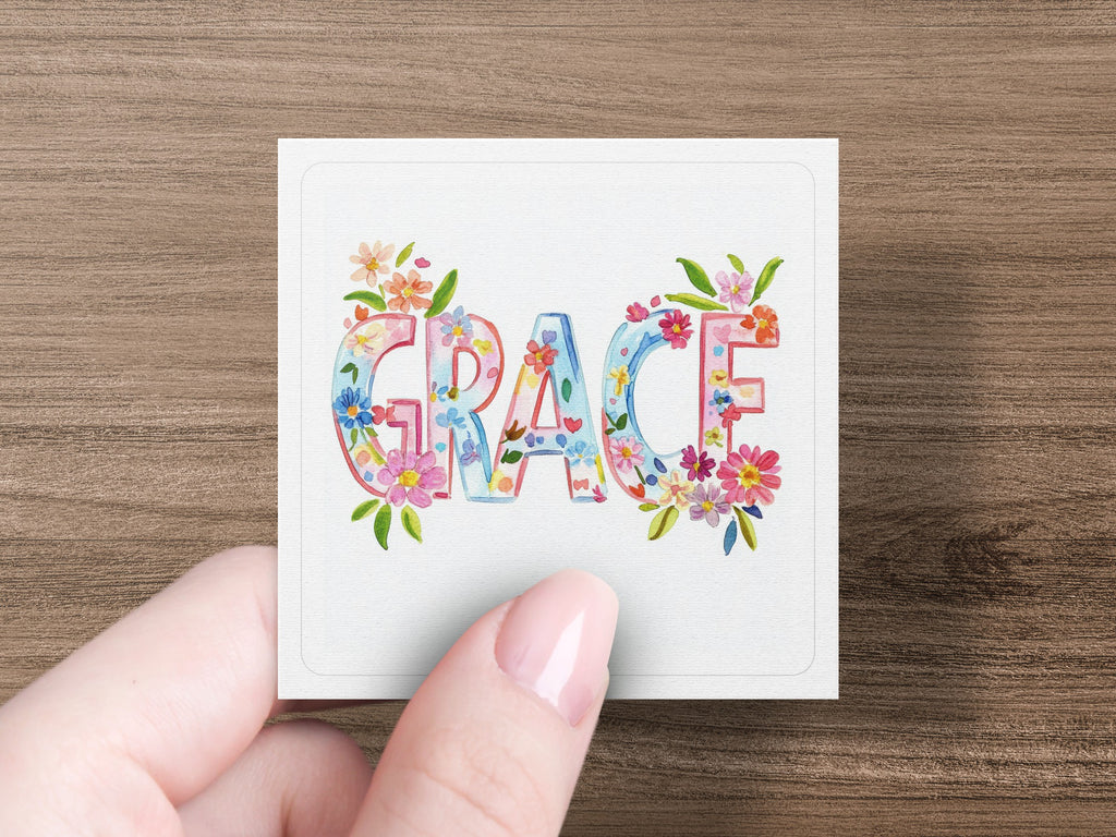 Hand holding square card with colorful floral letters spelling "GRACE".