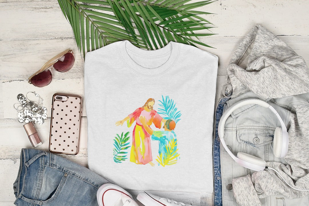 White t-shirt featuring watercolor art of Jesus embracing a person, surrounded by green leaves.