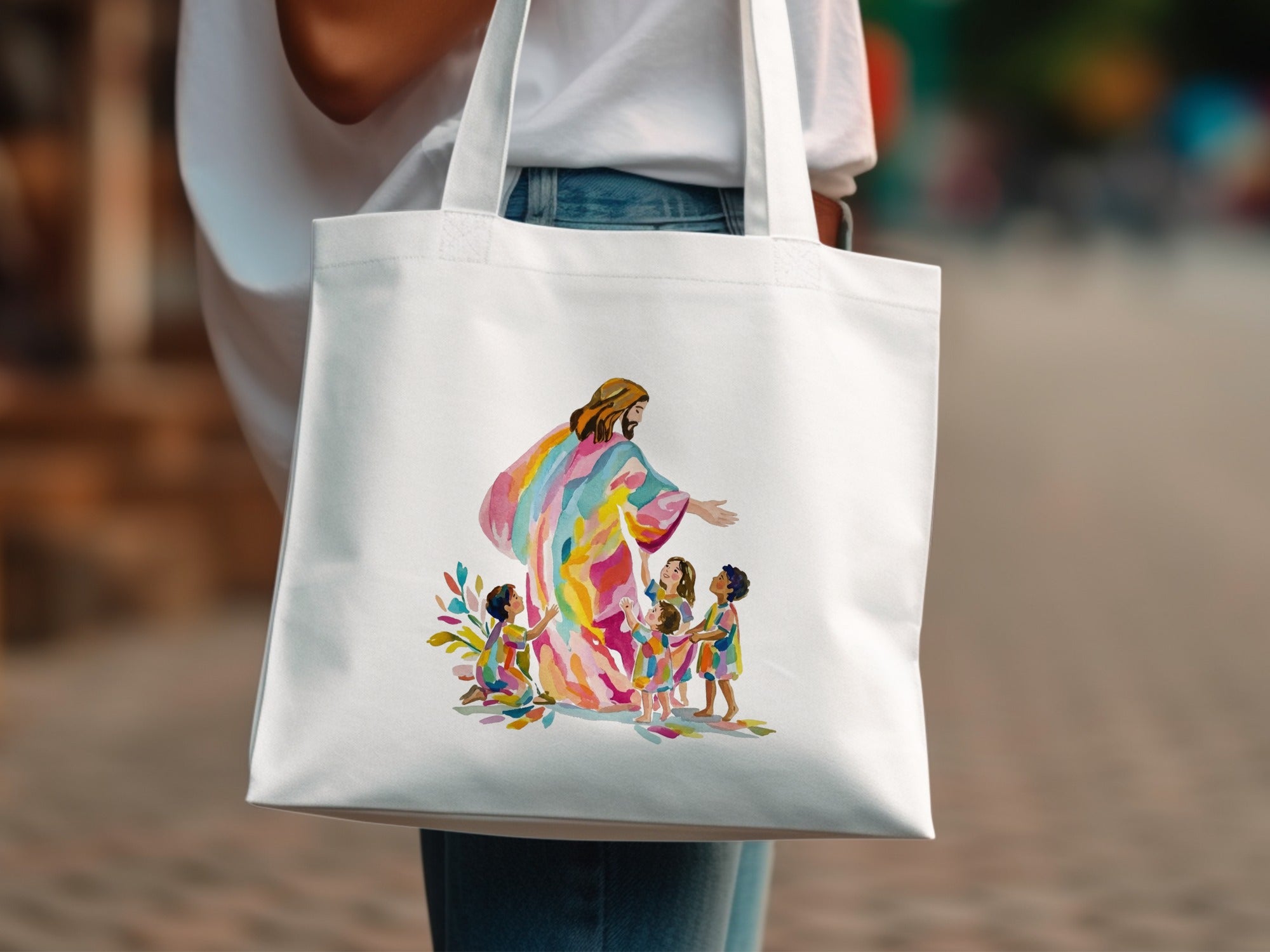 Jesus in colorful robes embracing children, watercolor illustration on a white tote bag.