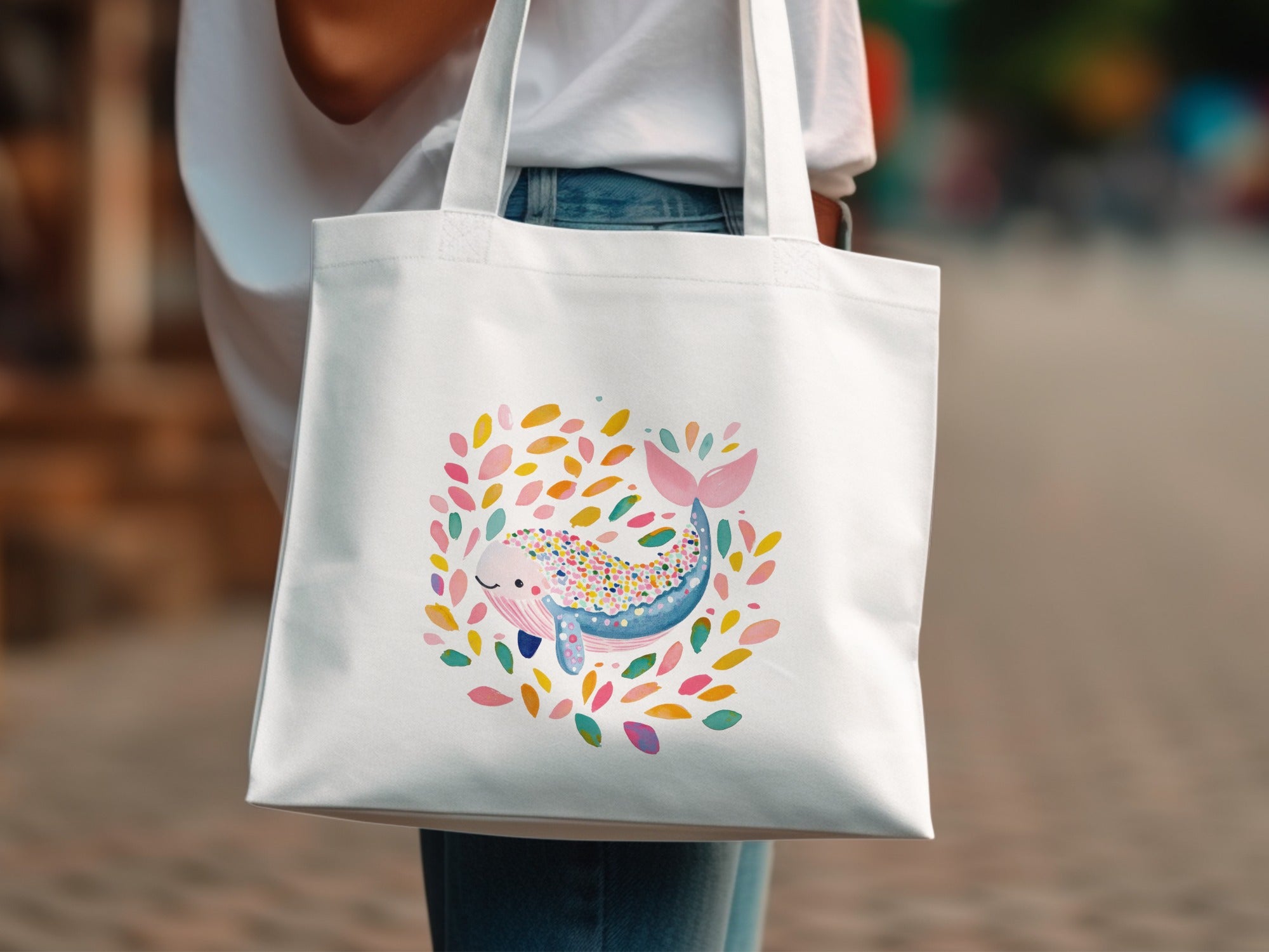 White tote bag with a watercolor illustration of a smiling whale surrounded by colorful leaves.