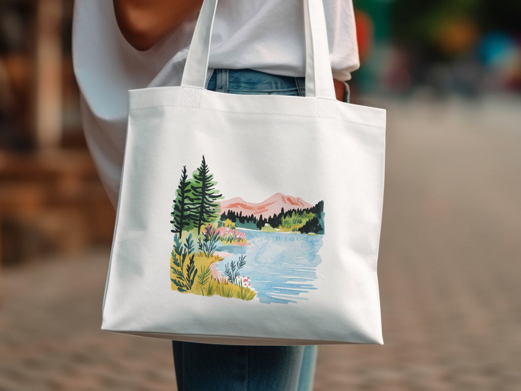 White tote bag with watercolor landscape of trees, lake, and mountains.