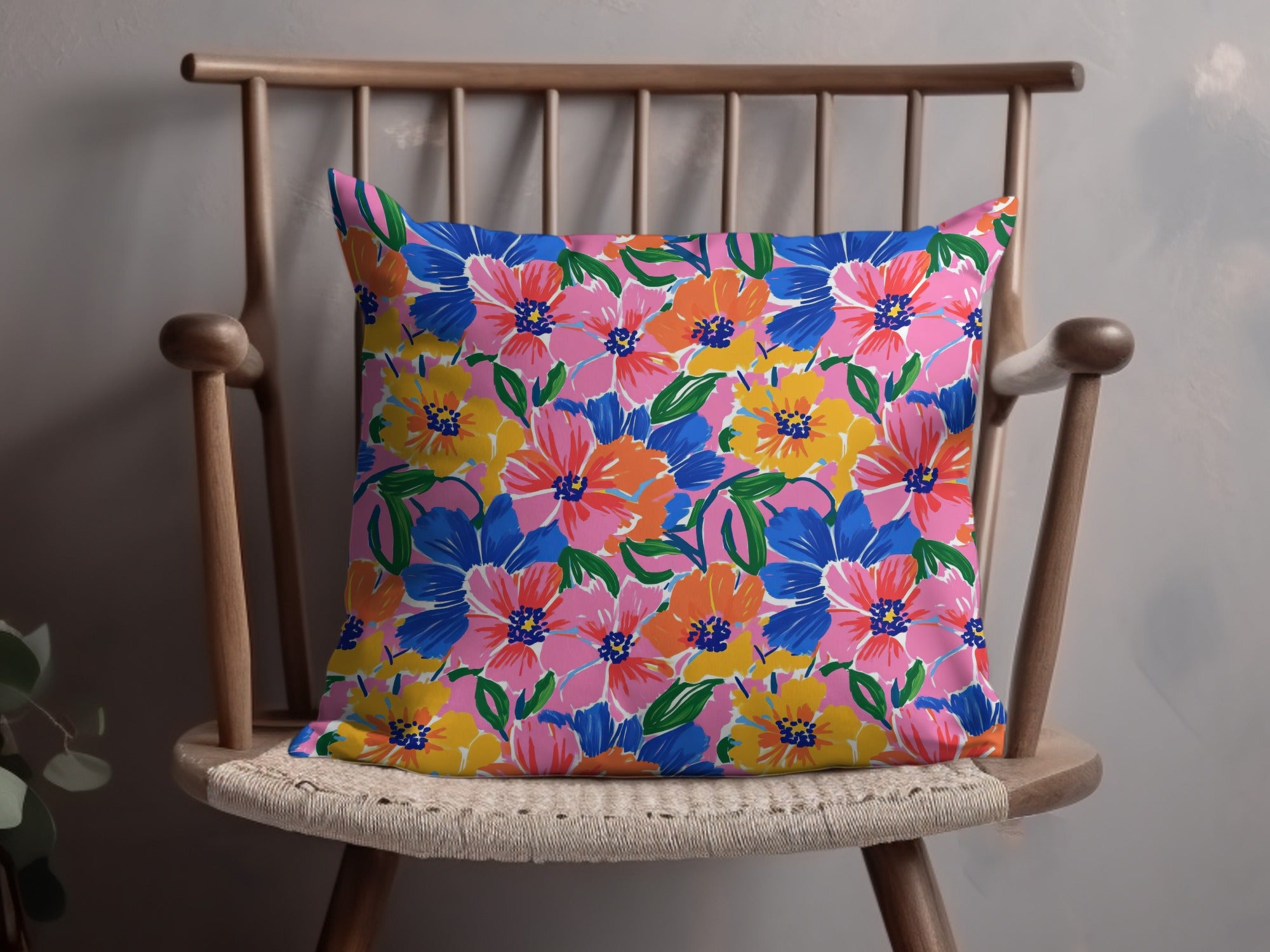 Floral throw pillow with pink, blue, orange, and yellow flowers on a wooden chair.