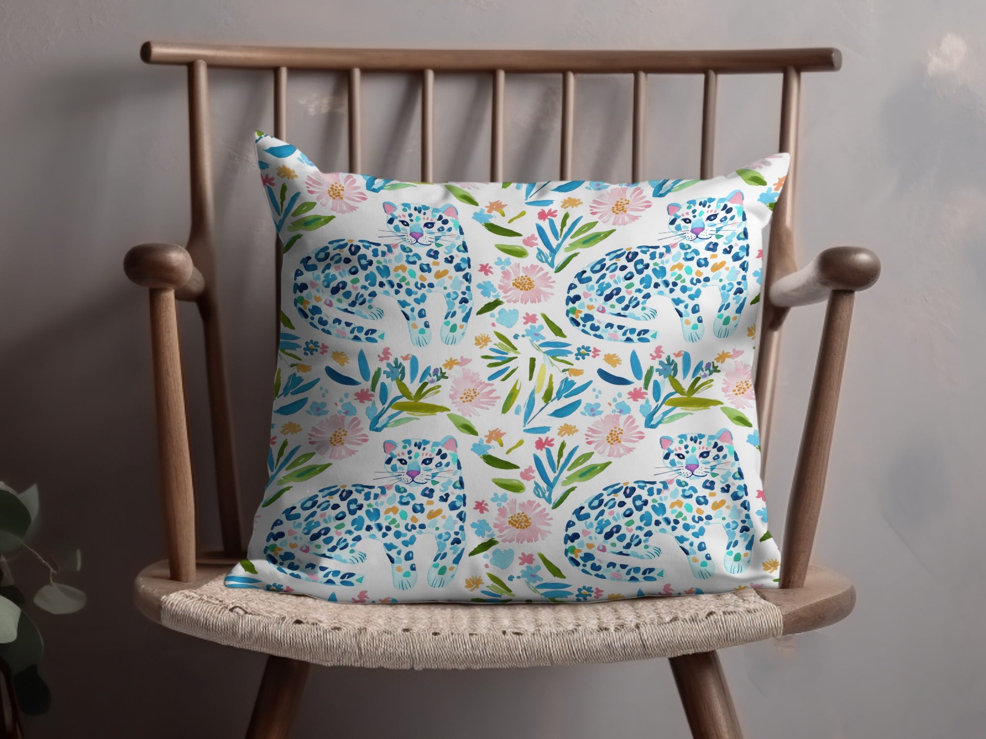 Watercolor pillow with leopards and floral pattern on a wooden chair.