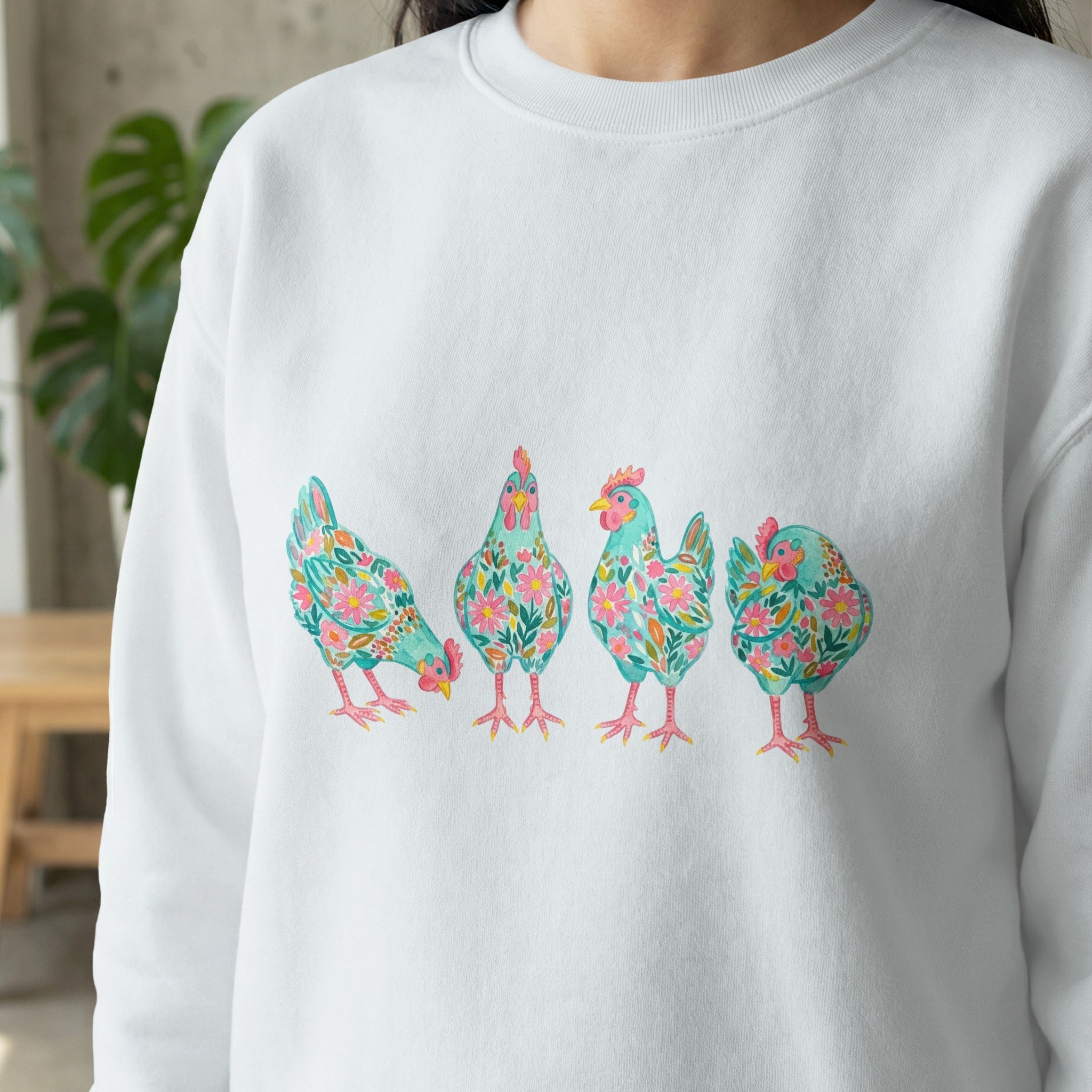 White sweatshirt with four colorful floral watercolor chickens across the chest.