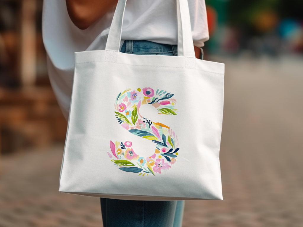 White tote bag with a colorful floral letter S design.