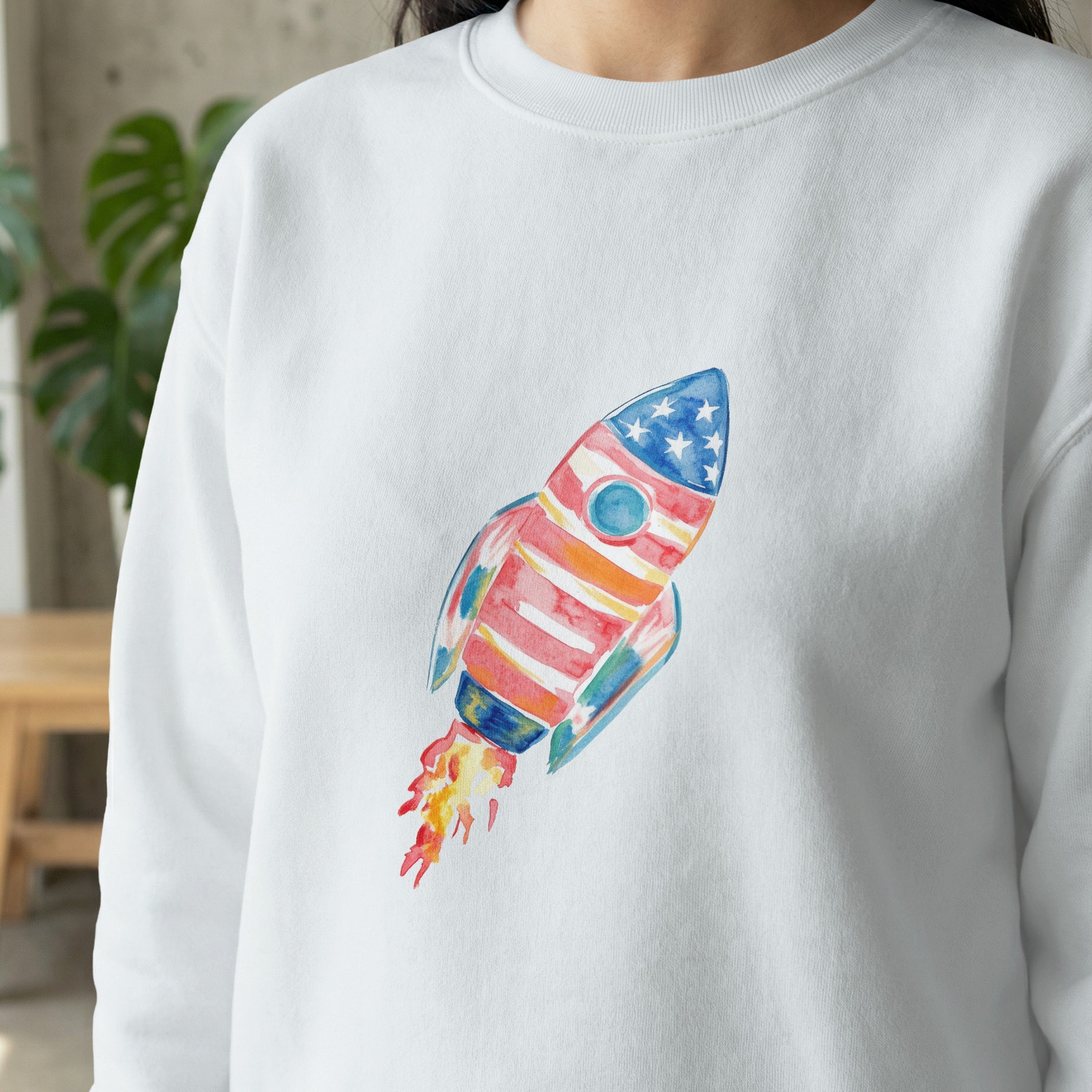 White sweatshirt with watercolor rocket ship design.