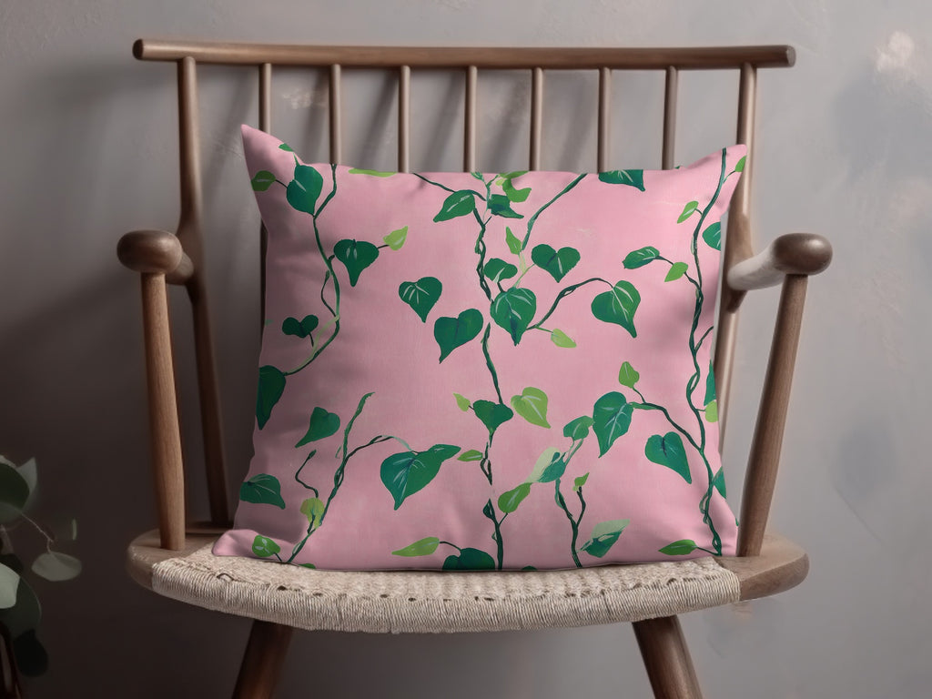 Pink throw pillow with green leafy vine pattern on a wooden chair.