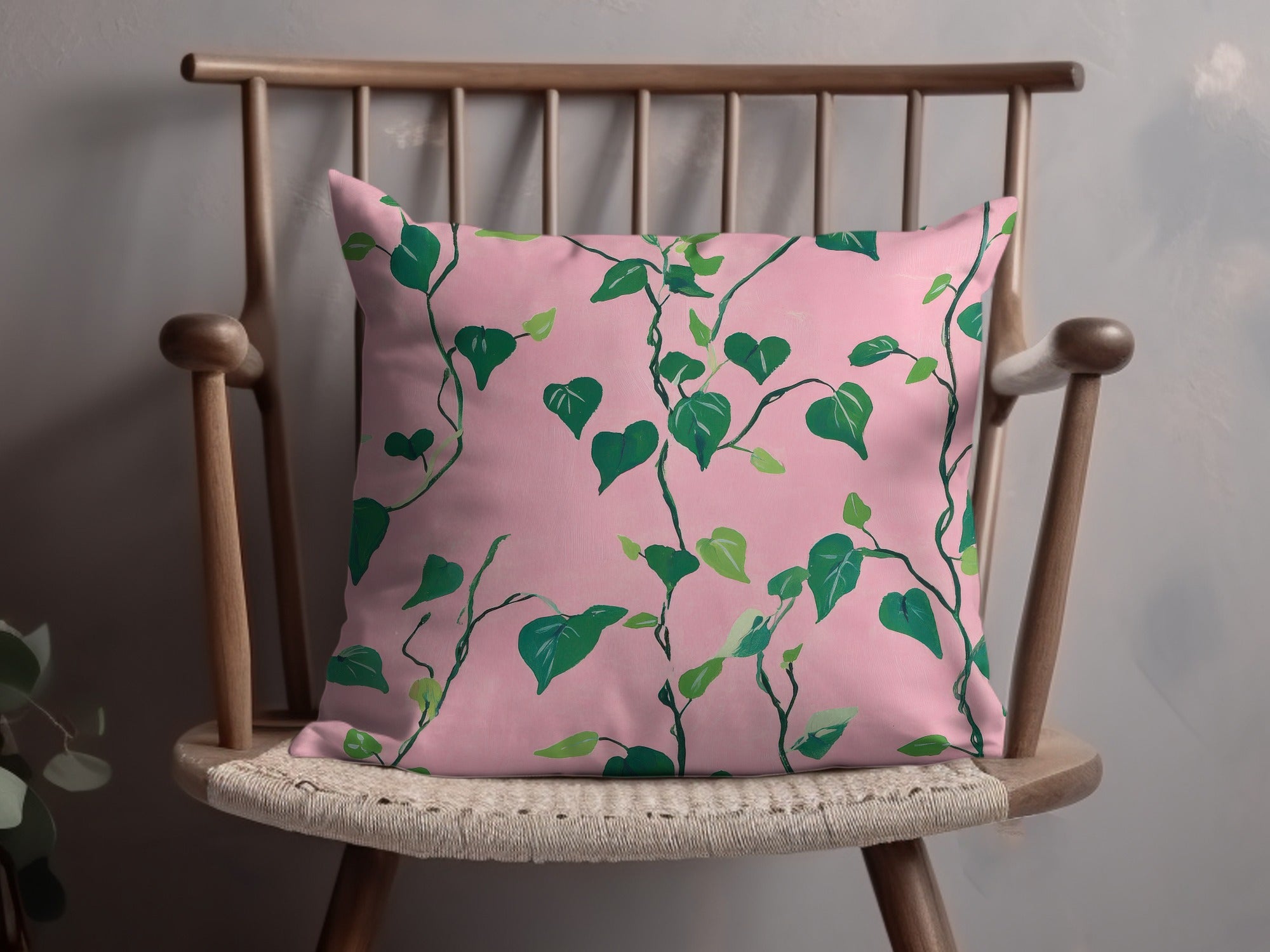 Pink throw pillow with green leafy vine pattern on a wooden chair.