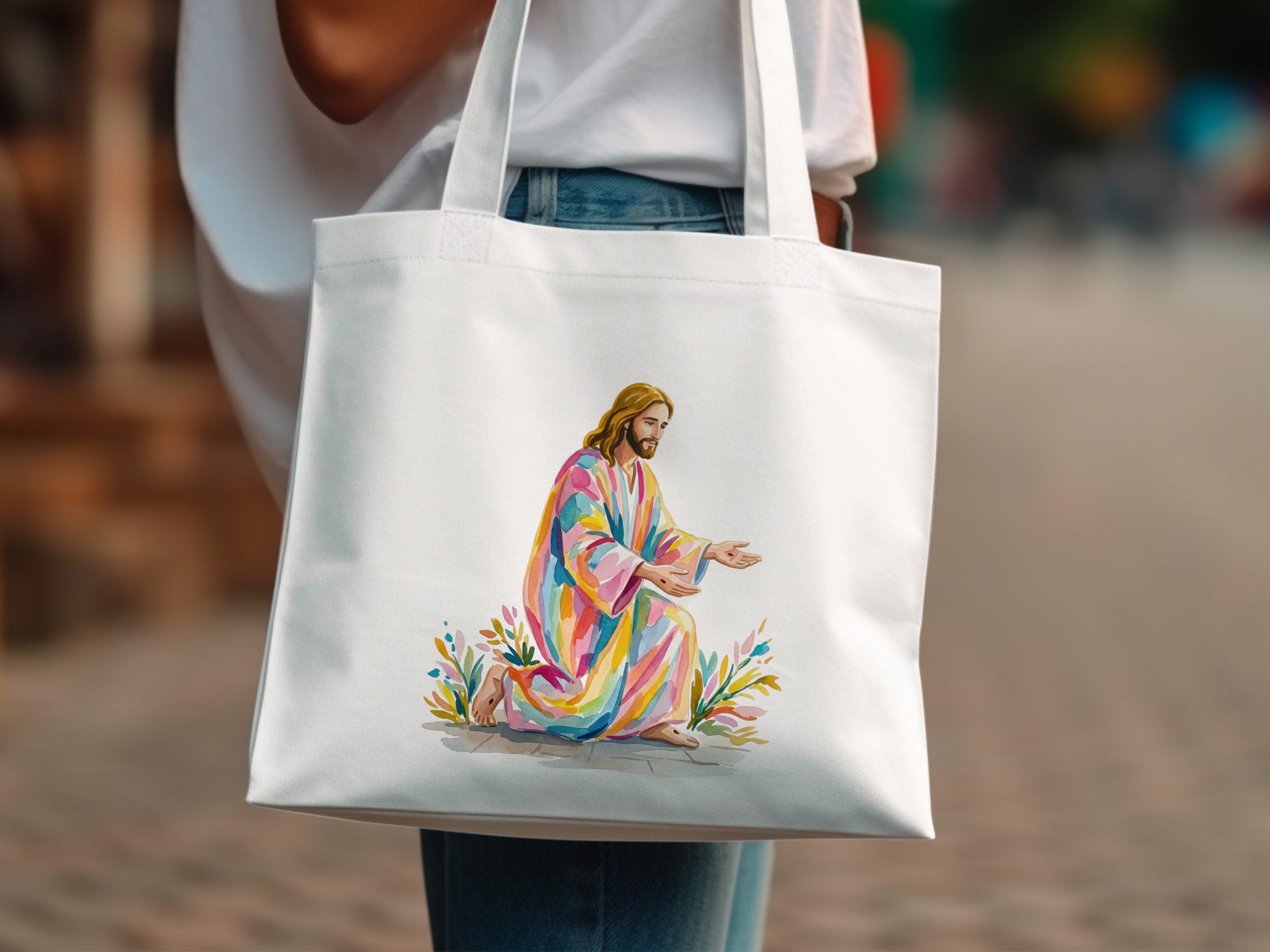 White tote bag with watercolor painting of Jesus in colorful robe kneeling.