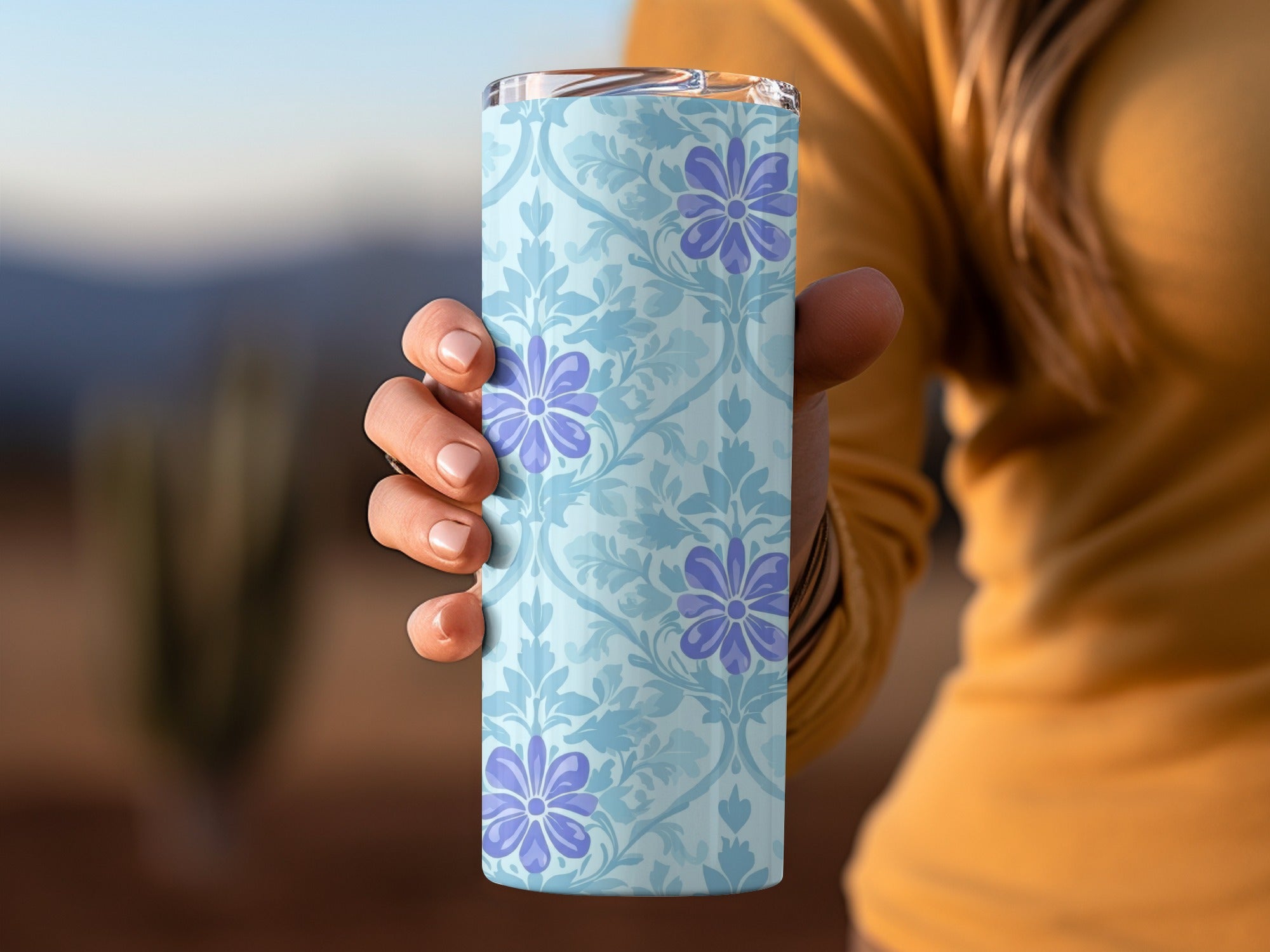 Light blue tumbler with purple floral pattern held by a hand.
