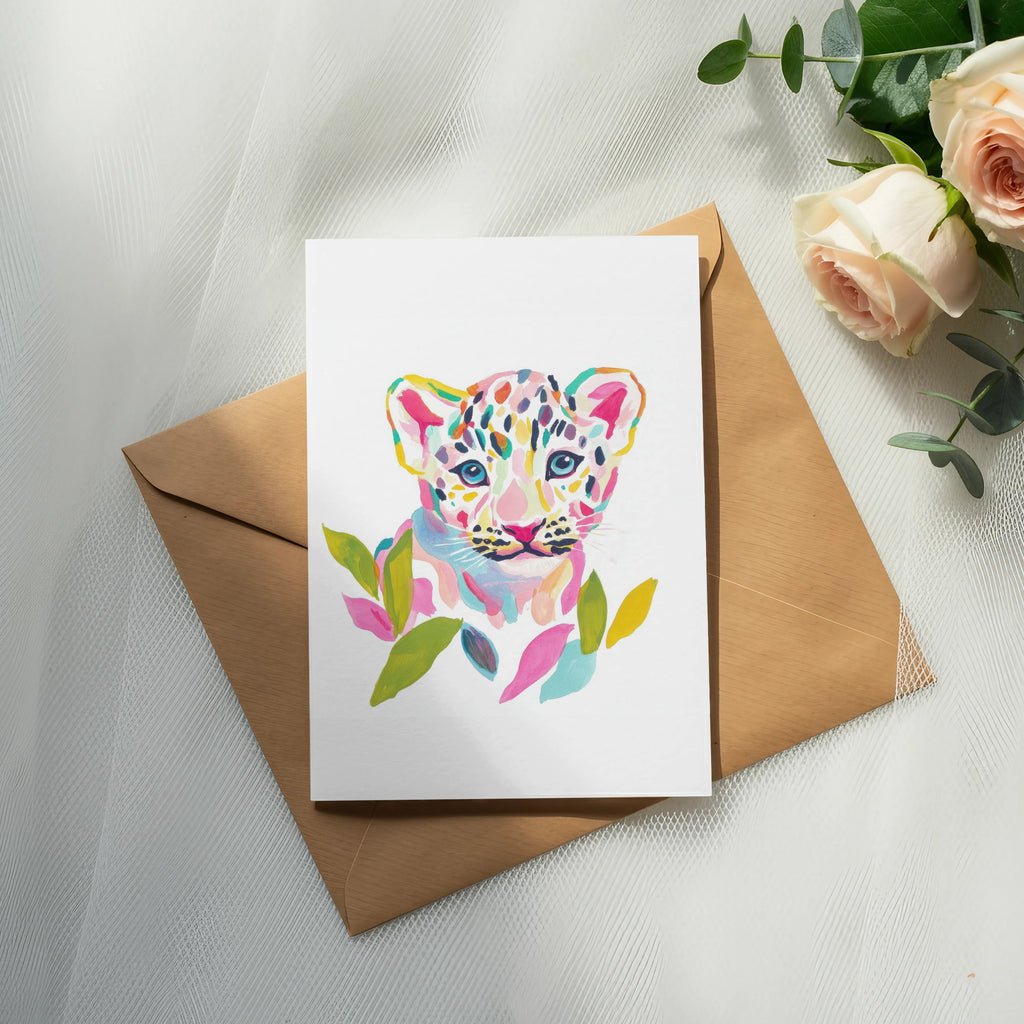 Watercolor painting of a colorful leopard cub on a card, resting on an envelope.