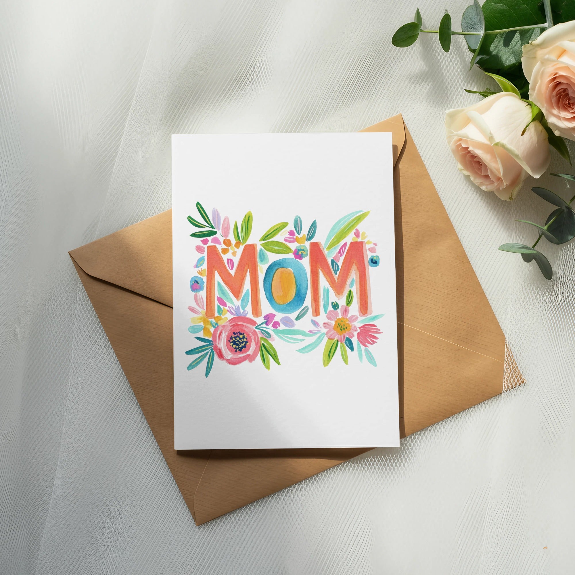 "MOM" in colorful floral lettering on a white card, atop a brown envelope.