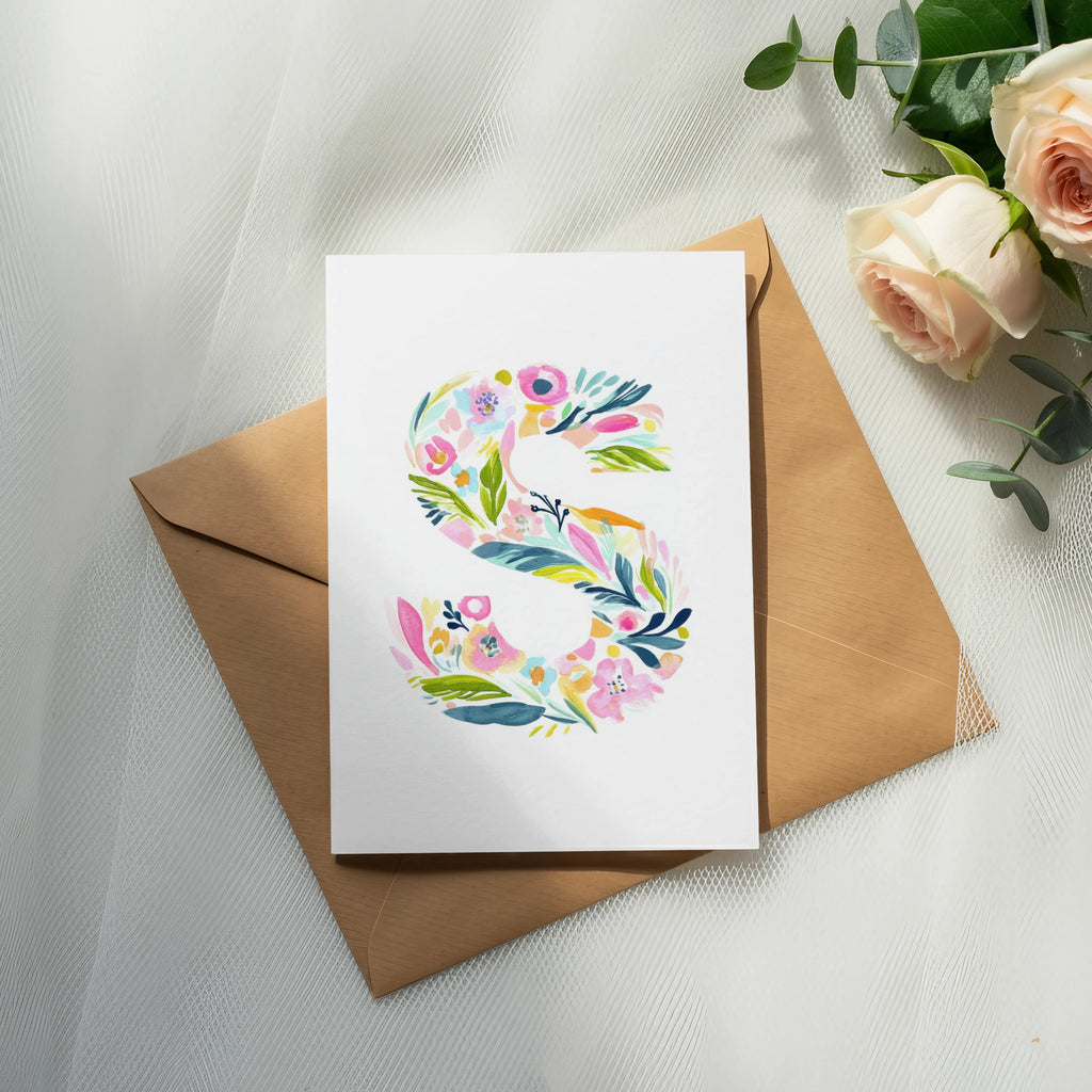 Floral letter S on a white card with a brown envelope and roses.