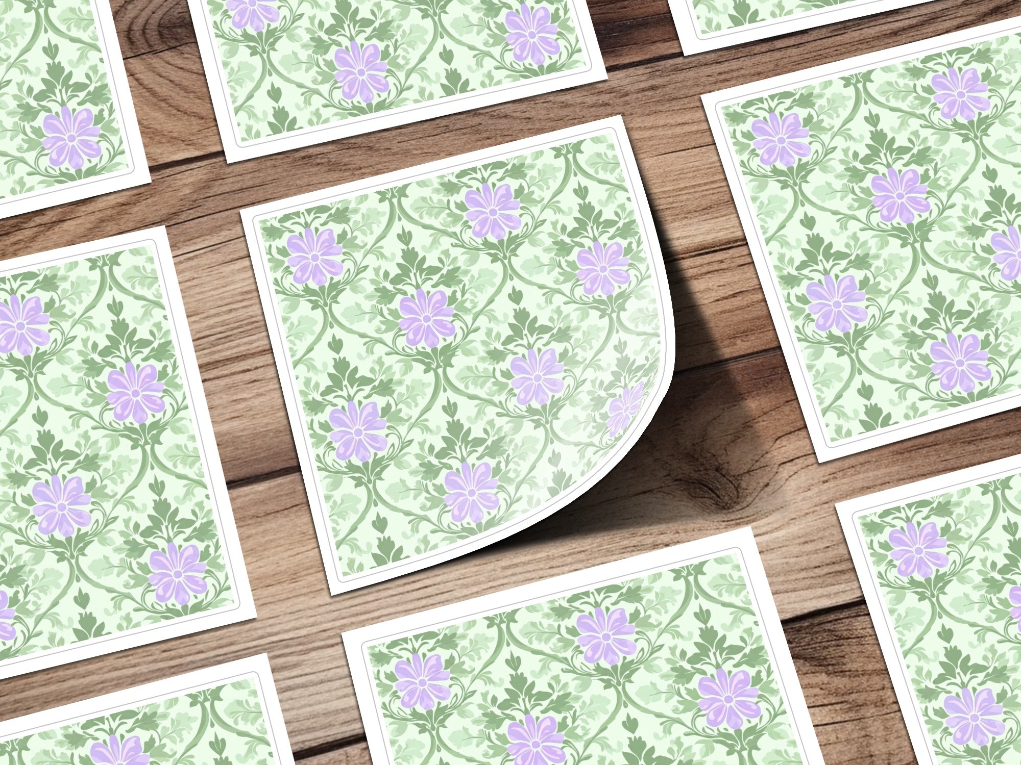 Green floral pattern with purple flowers on paper squares scattered on wood.