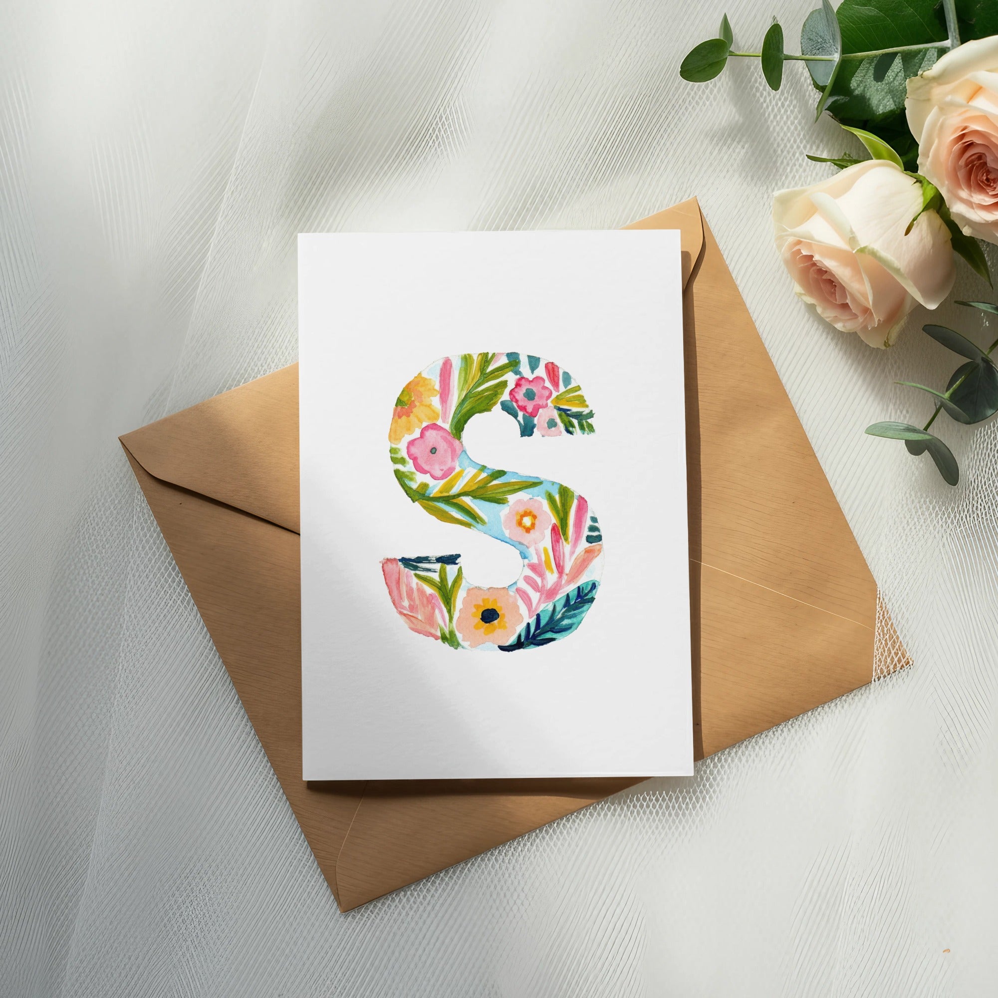 Watercolor letter "S" with floral design on a card with envelope and roses.