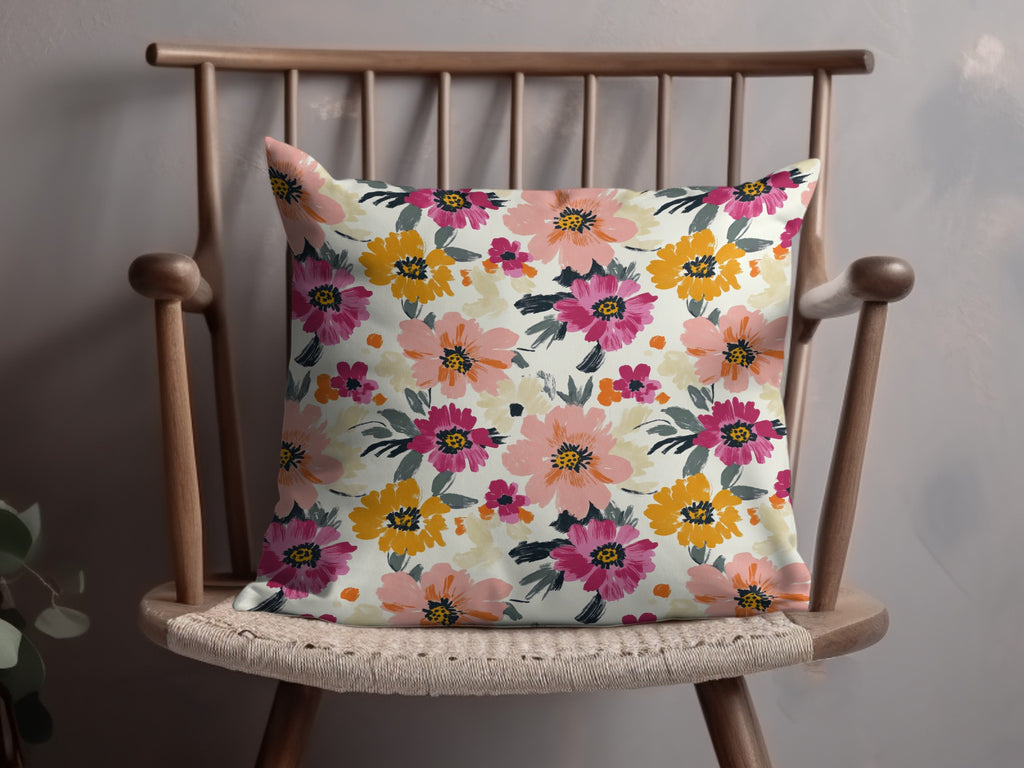 Floral accent pillow with pink, yellow, and orange flowers on a light background.
